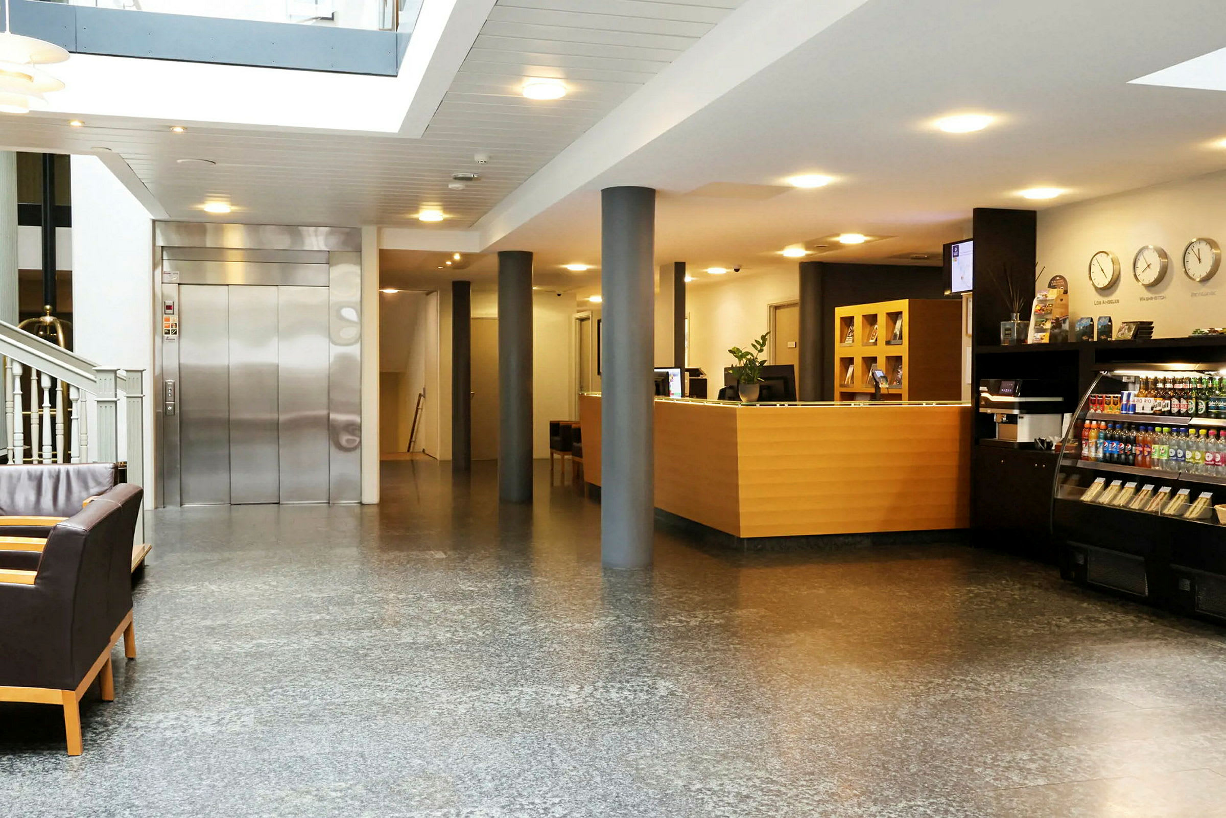 Ett hotellreceptionsområde med en reception, en hiss, soffor och en liten butik. (AI-genererad text)