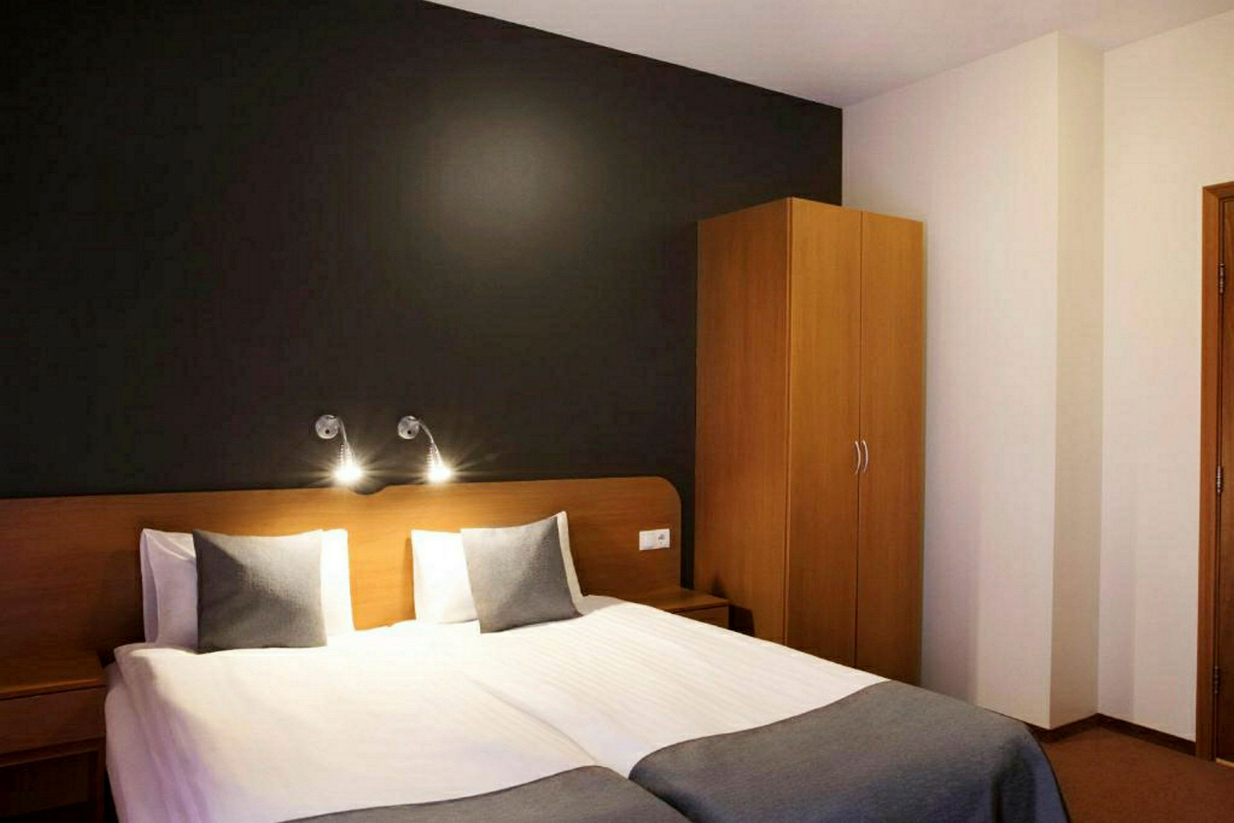 Bild av ett hotellrum med två enkelsängar, mörk vägg bakom, och en träfärgad garderob till höger. (AI-genererad text)