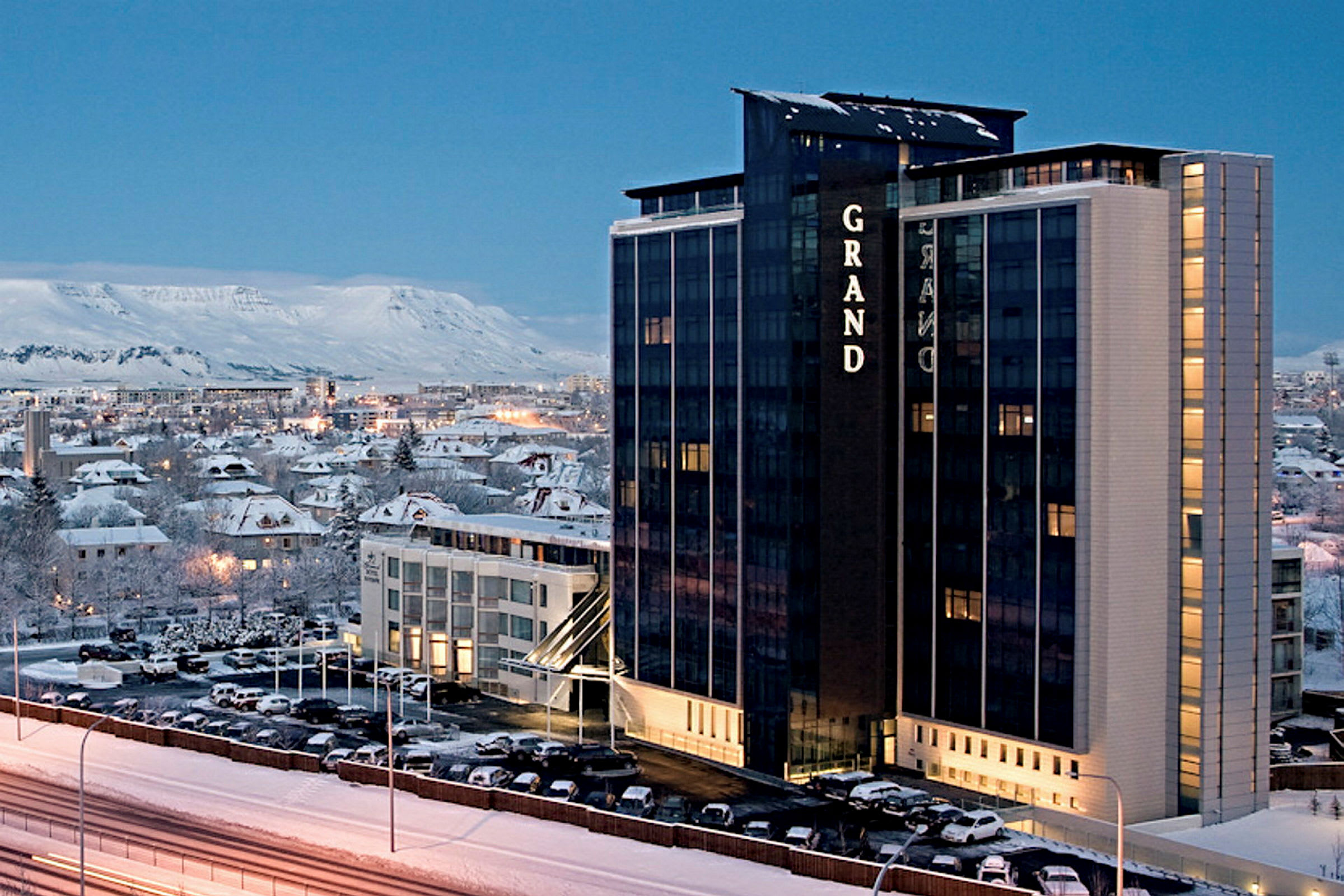 Ett höghushotell i vintrig miljö med en stad och berg i bakgrunden. (AI-genererad text)