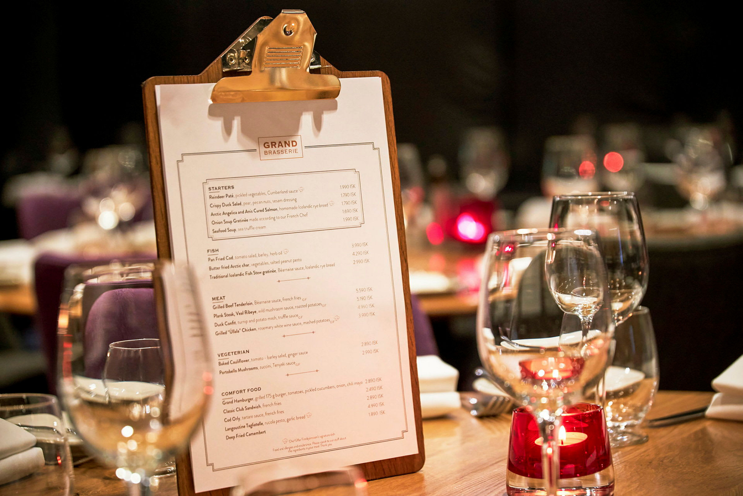 Ett bord på en restaurang med ett menyblad på en clipboard och glas med bordsdekoration. (AI-genererad text)