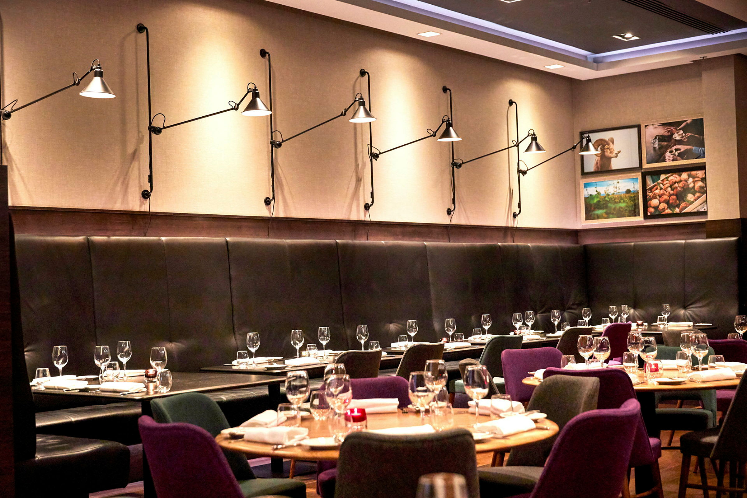 En modern restaurang med uppdukade bord och stolar, samt väggbelysning på en klädd vägg. (AI-genererad text)