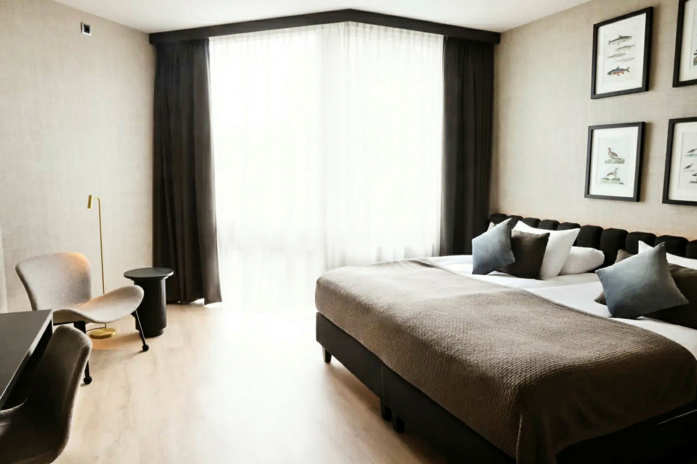 Ett hotellrum med en dubbelsäng, sittmöbler och ett stort fönster med ljusa gardiner. (AI-genererad text)