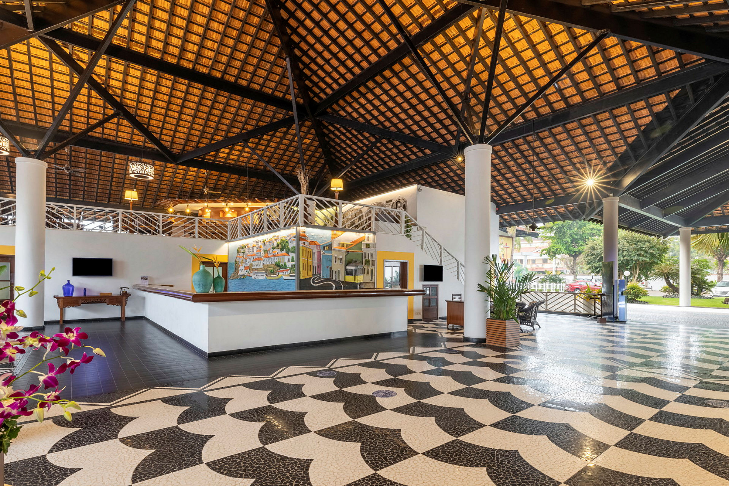 Hotellobby med en hög träpanelad takstruktur, färgglad konst på väggar, stora pelare och elegant mönstrat golv. (AI-genererad text)