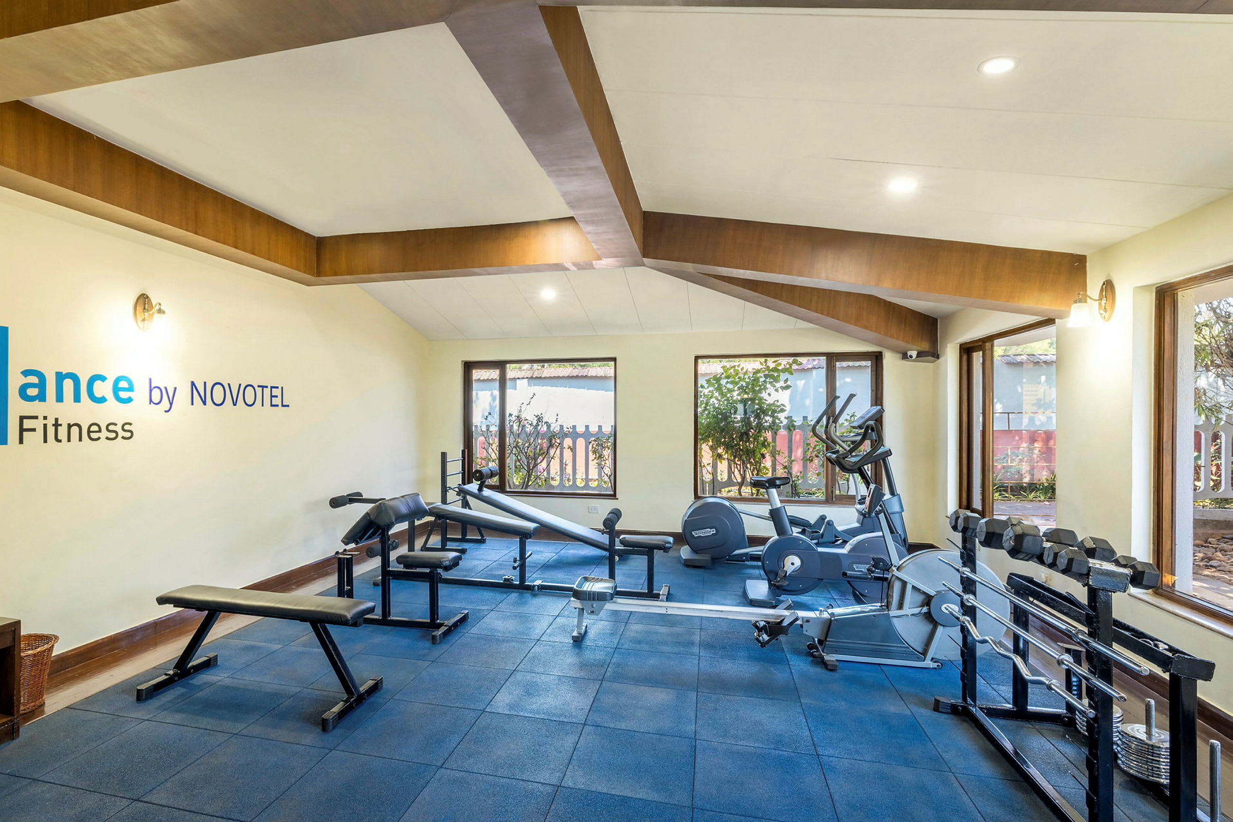 Ett gym med träningsutrustning, fönster och skylt med texten 'Balance by NOVOTEL Fitness'. (AI-genererad text)