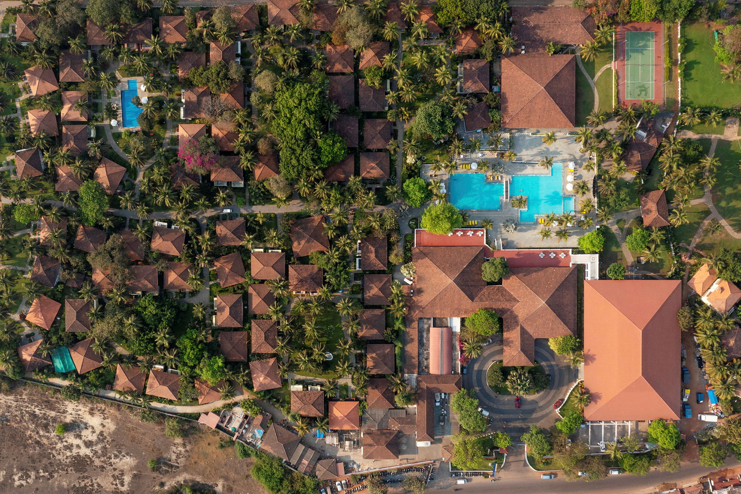 En flygbild som visar en resort med terrakottatak, grönområden, pooler och tennisbanor. (AI-genererad text)