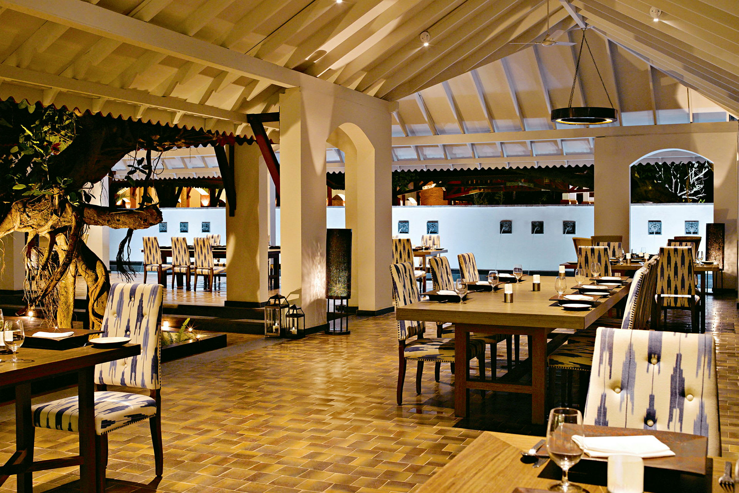 Interiören av en restaurang med sittplatser vid dukade bord och en trädtavla i mitten. (AI-genererad text)