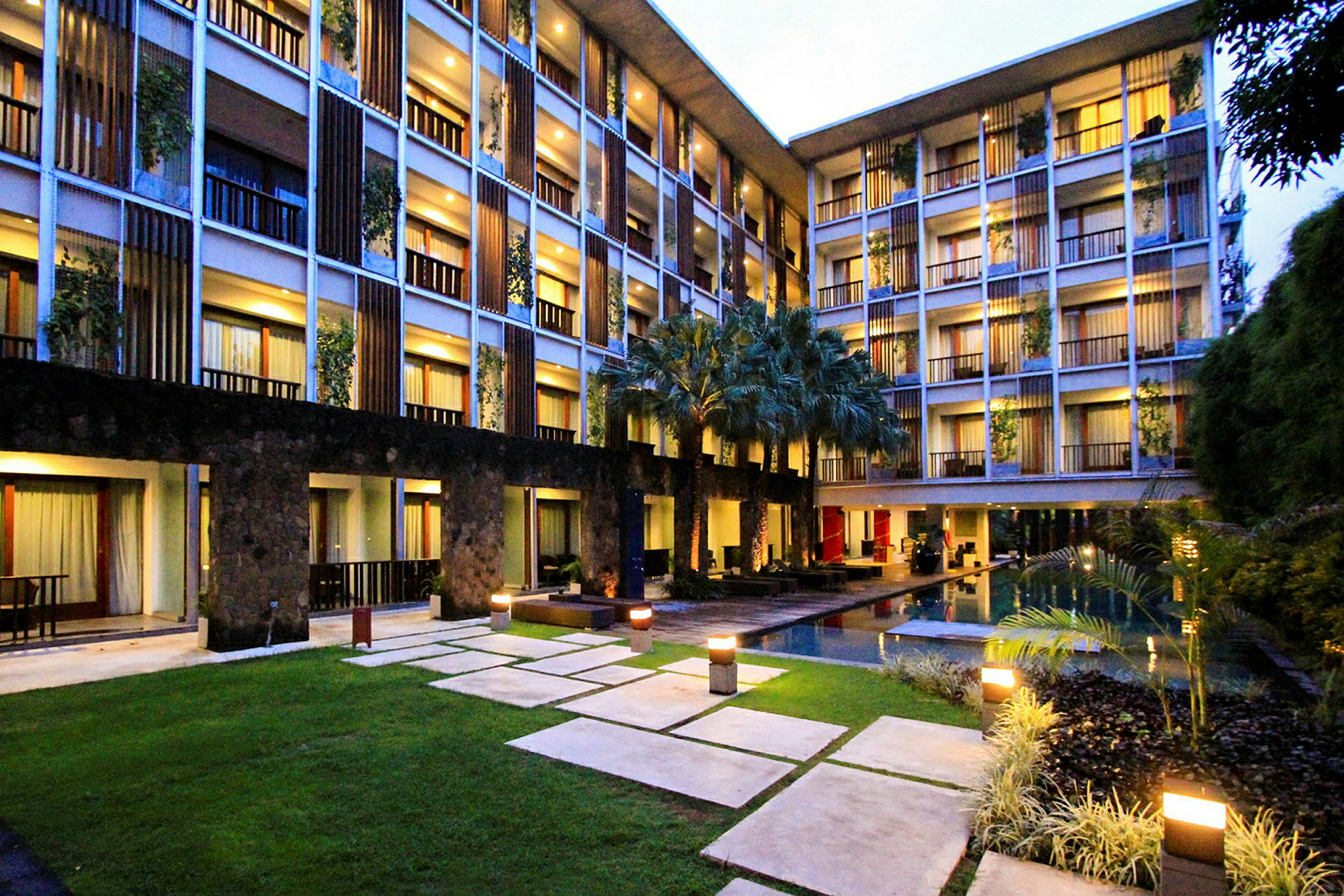 Ett modernt hotell med flera våningar runt en innergård med grönska och en pool. (AI-genererad text)