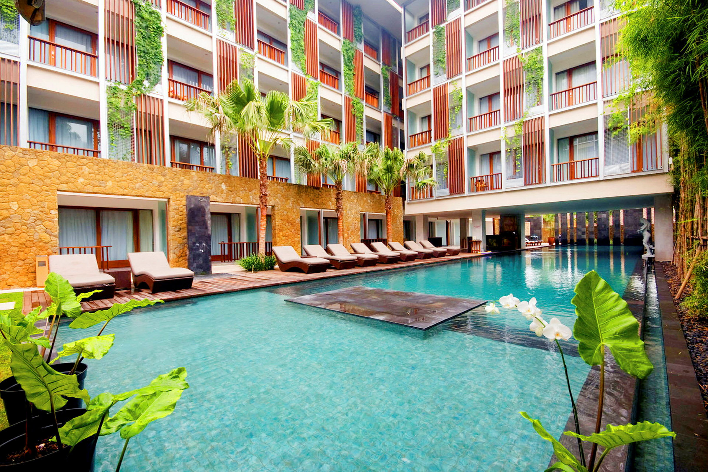 Ett hotell med en modern pool och omgivande solsängar samt grönska. (AI-genererad text)