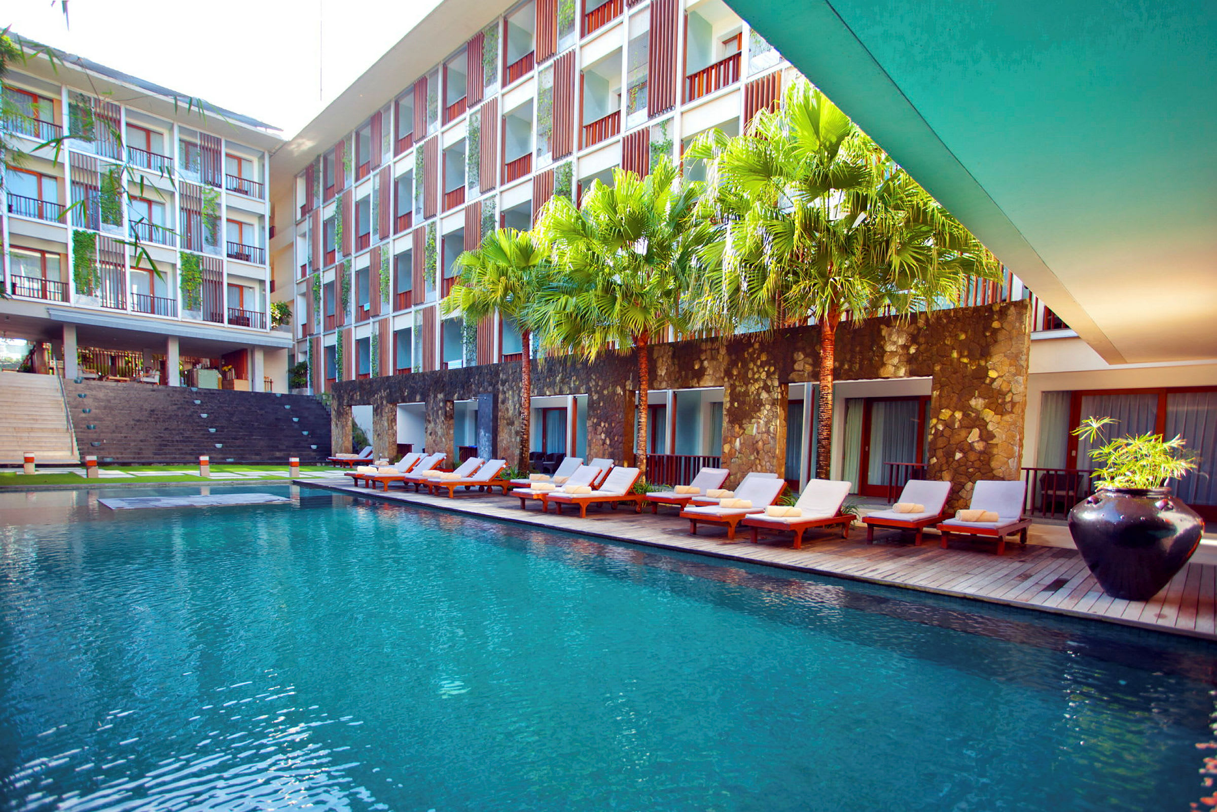 Ett modernt hotellområde med en stor pool, solstolar och gröna palmer. (AI-genererad text)