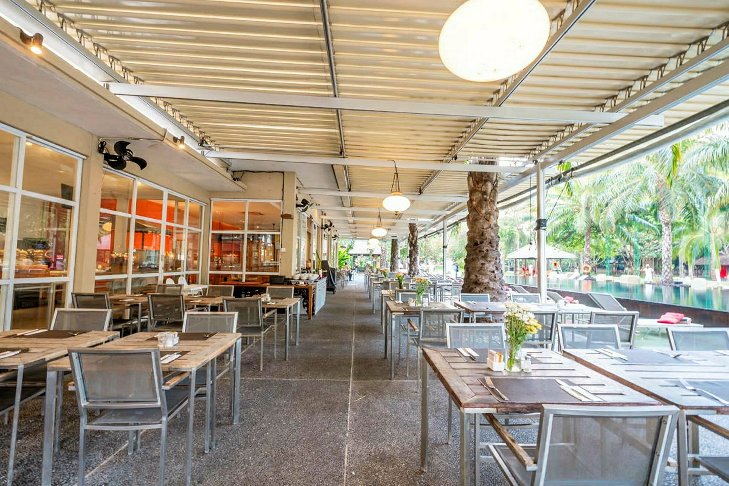En utomhusrestaurang med bord och stolar som är uppställda under ett täckt tak. (AI-genererad text)