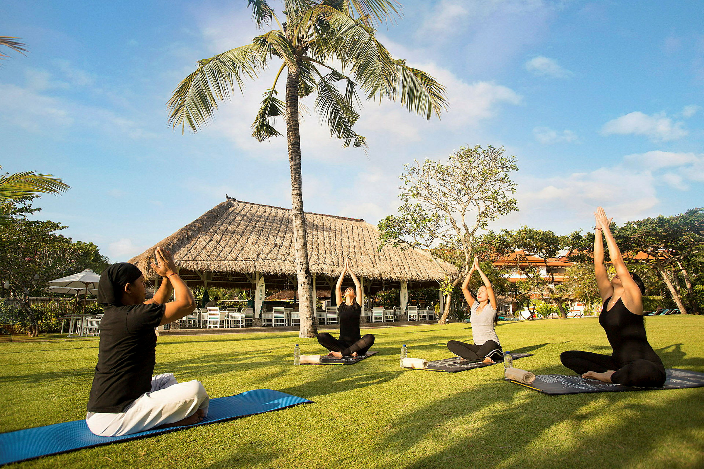 Personer utövar yoga på en gräsmatta med en tropisk bakgrund. (AI-genererad text)