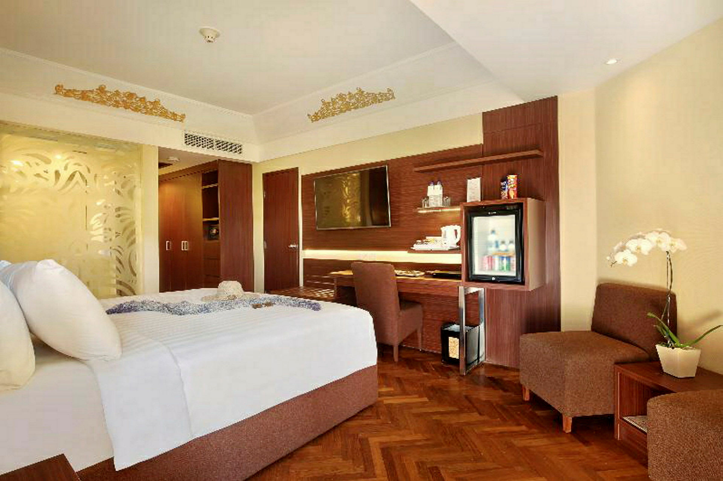 Ett hotellrum med en stor säng, en skrivbordshörna, en TV monterad på väggen och en minibar. Inredningen är i ljusa färger med inslag av trä. (AI-genererad text)