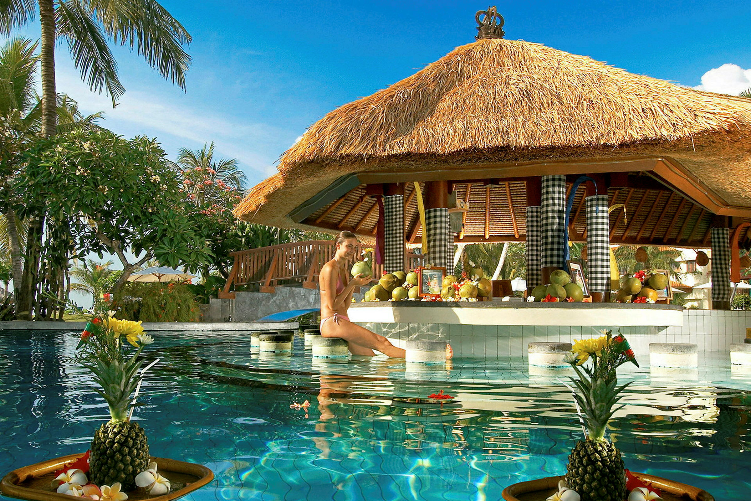 Bild av en poolbar med halmtak och ett bord dekorerat med frukter, samt en uppställd ananas i förgrunden. (AI-genererad text)