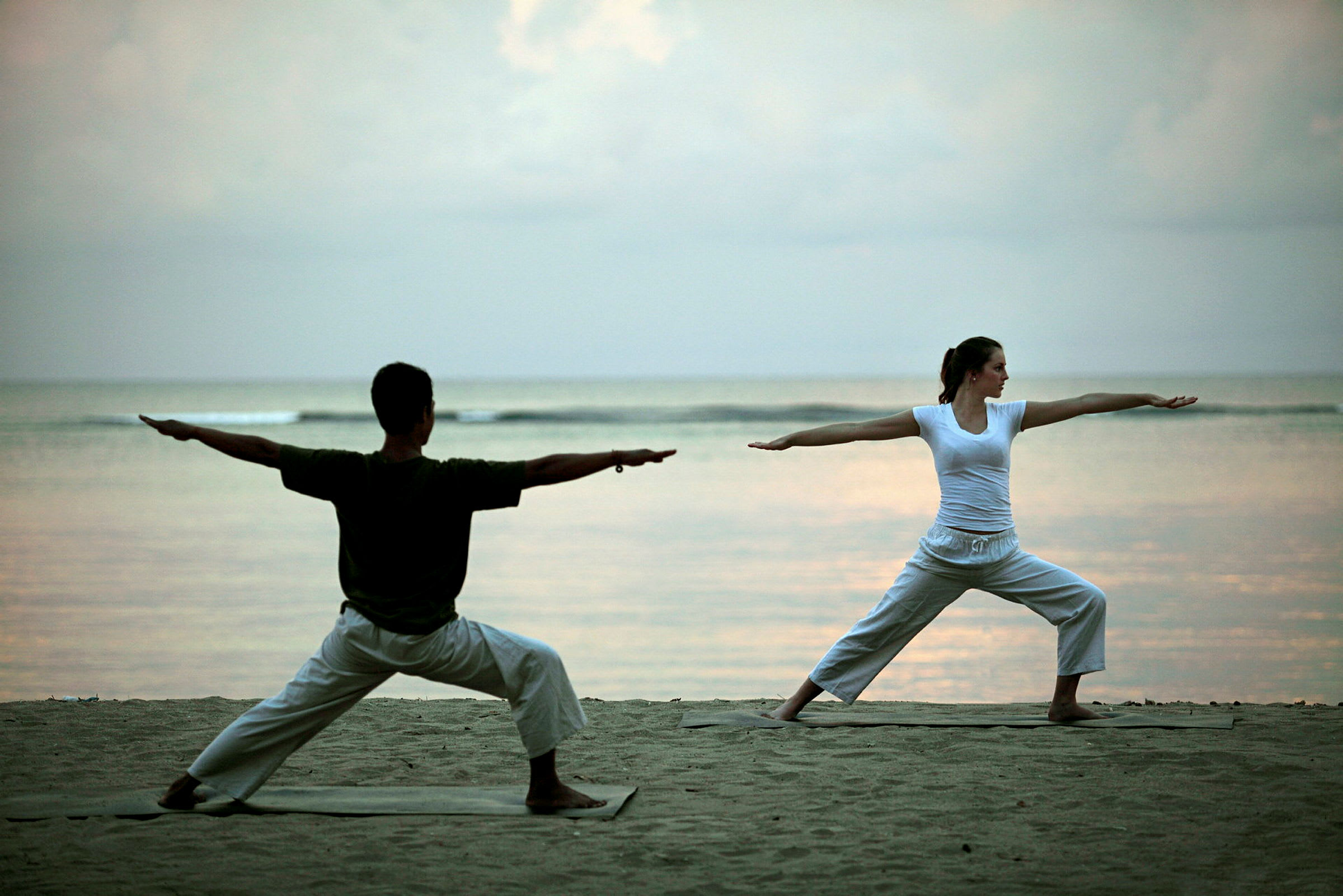 Två personer utför yogaposer på stranden med havet i bakgrunden. (AI-genererad text)