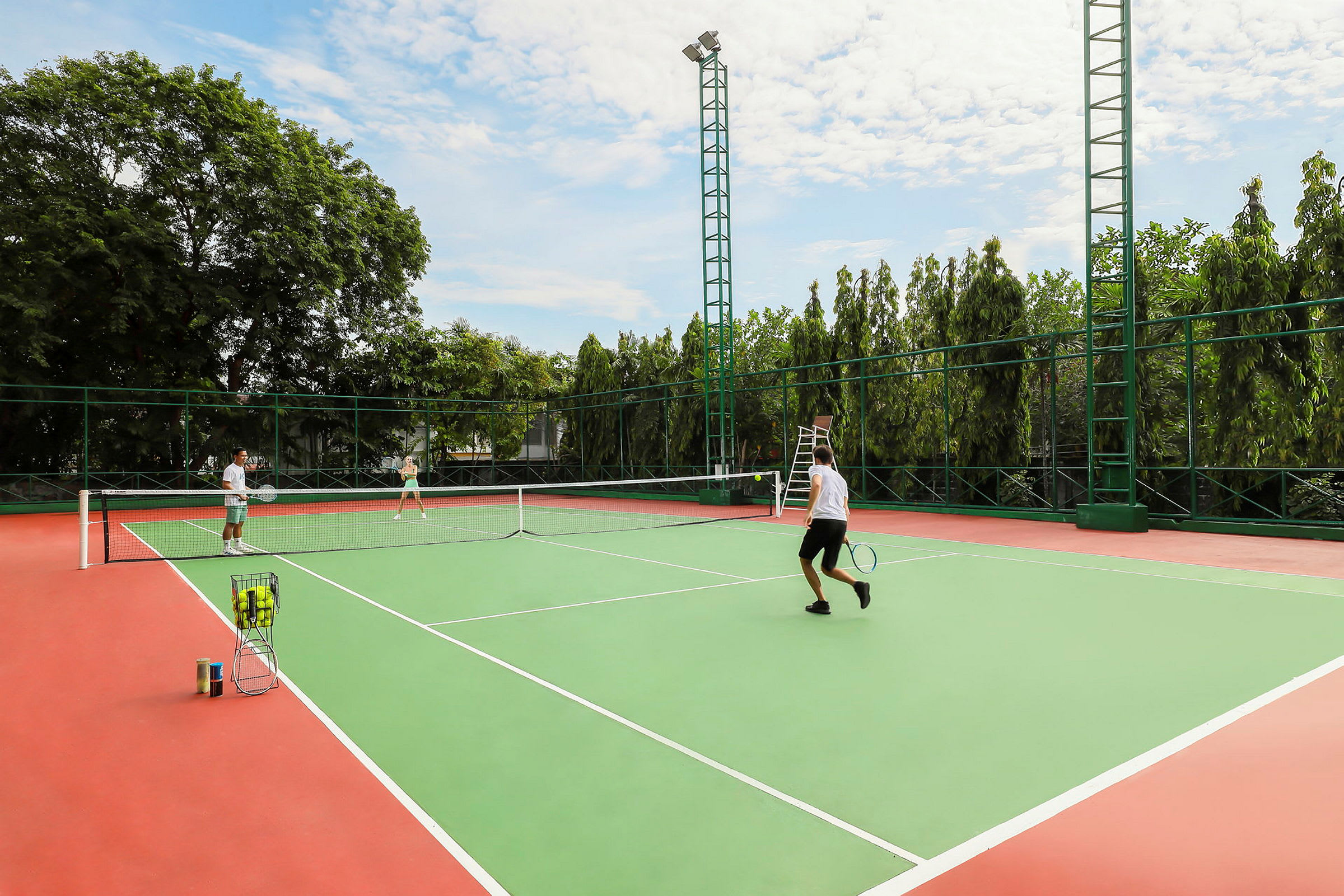 Personer spelar tennis på en utomhusbana. I bakgrunden syns träd. (AI-genererad text)