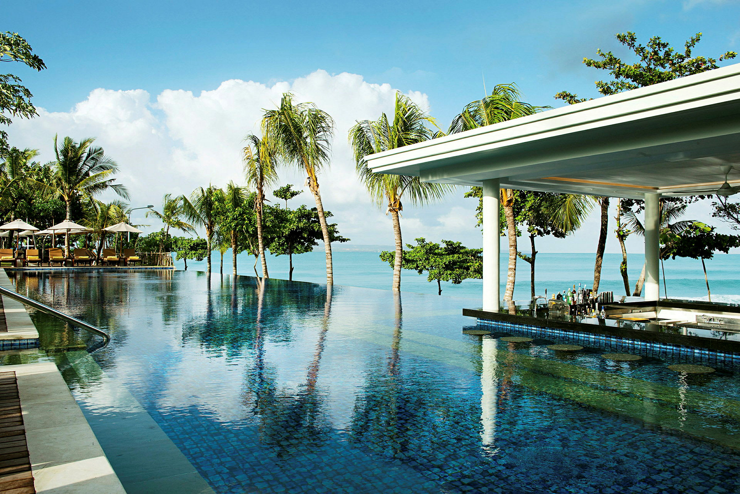 En infinitypool vid stranden med palmer i bakgrunden och en bar under ett tak intill poolen. (AI-genererad text)