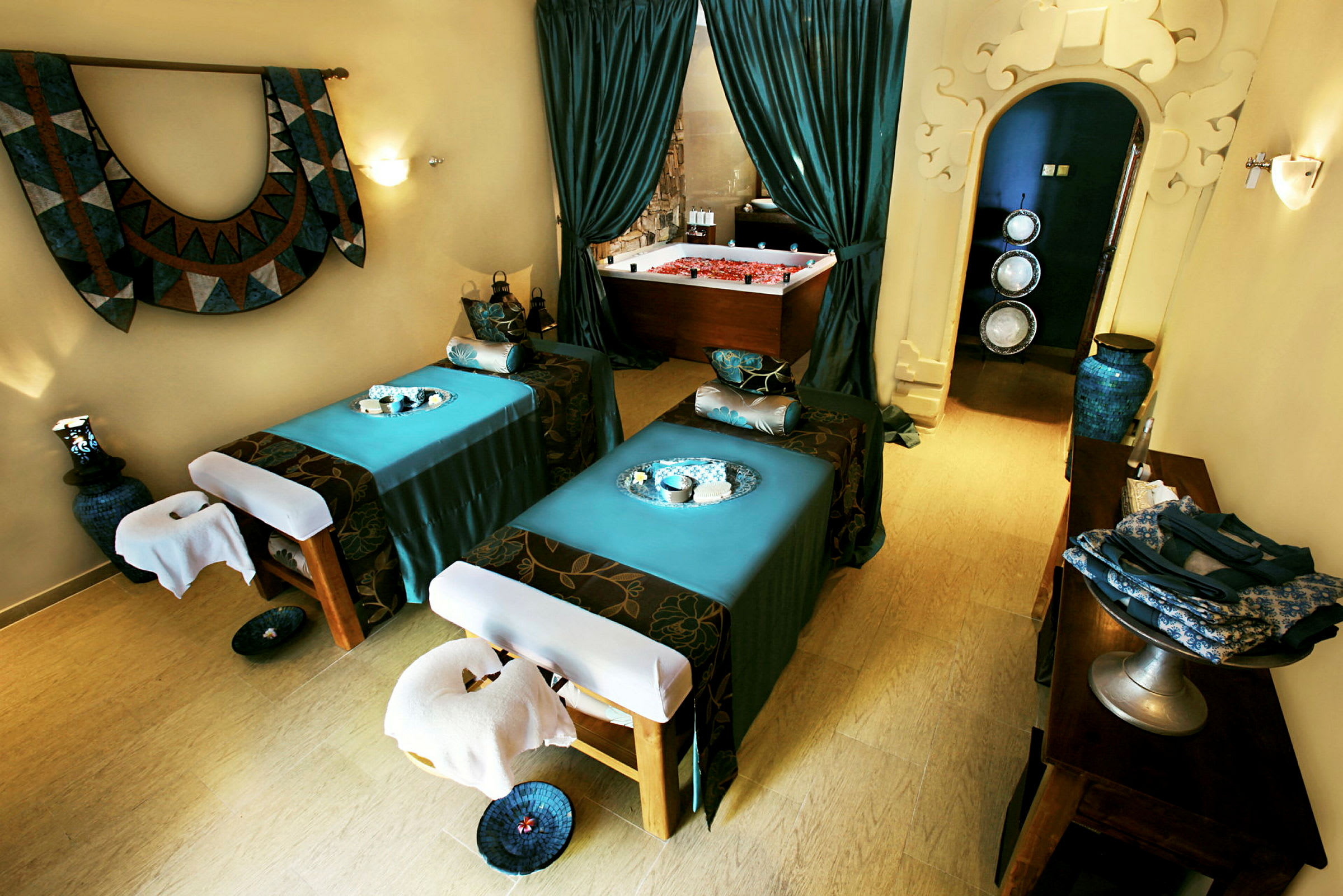 Bild på ett mysigt spa-rum med två massagebänkar och en dekorativ jacuzzi i bakgrunden. (AI-genererad text)