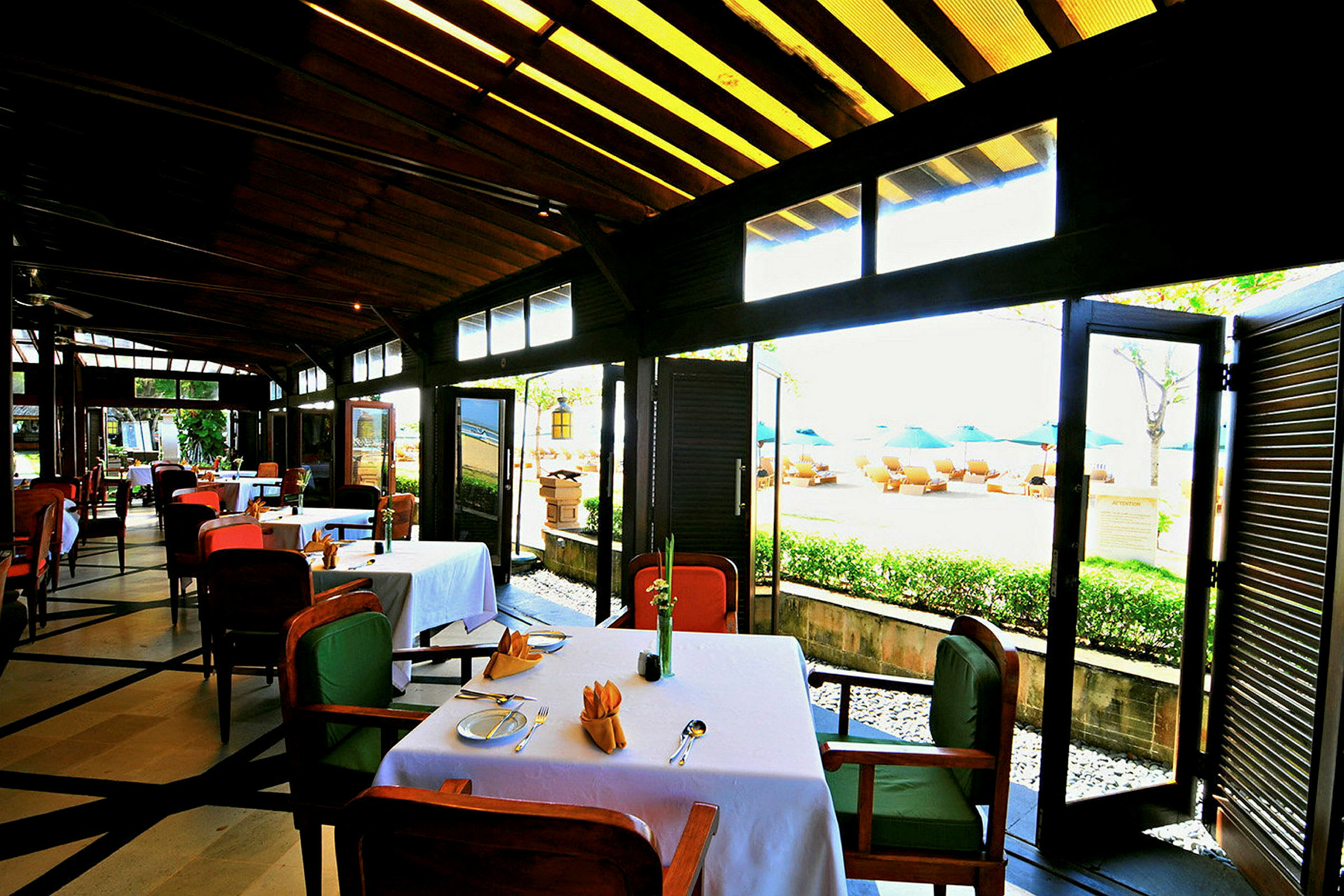 En restaurang med dukade bord, stolar och utsikt mot en strand med solstolar och parasoll. (AI-genererad text)