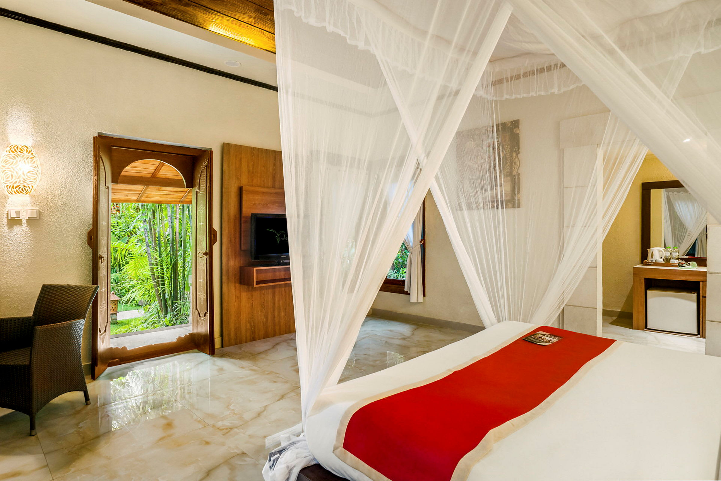 Ett rum med en säng inklädd i ett vitt myggnät, en röd löpare på sängen, en öppen dörr som leder ut till en grönskande miljö och modern inredning. (AI-genererad text)