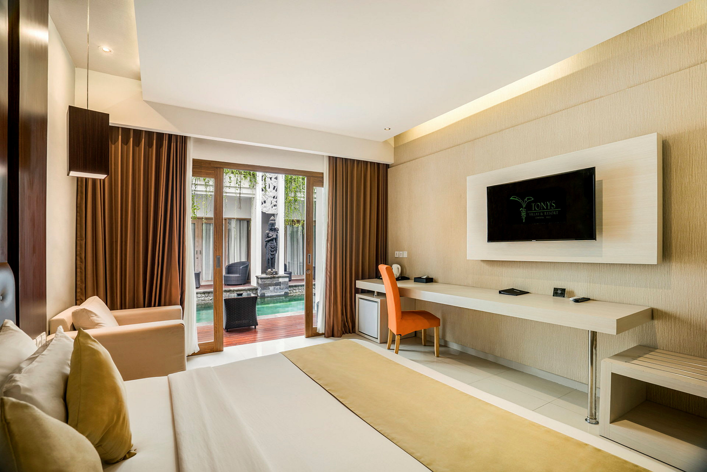 Ett hotellrum med en säng, skrivbord med stol, väggmonterad TV och en glaspanel som visar en utomhuspool. (AI-genererad text)