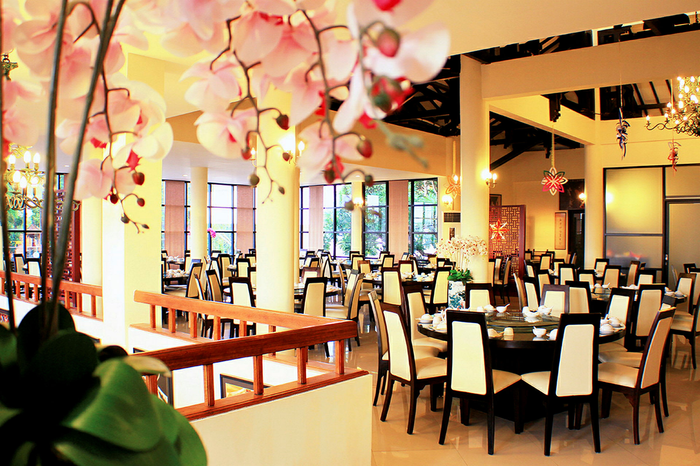 En elegant inredd restaurang med runda bord omgivna av stolar med ljusa ryggstöd, och dekorativa blommor i förgrunden. (AI-genererad text)