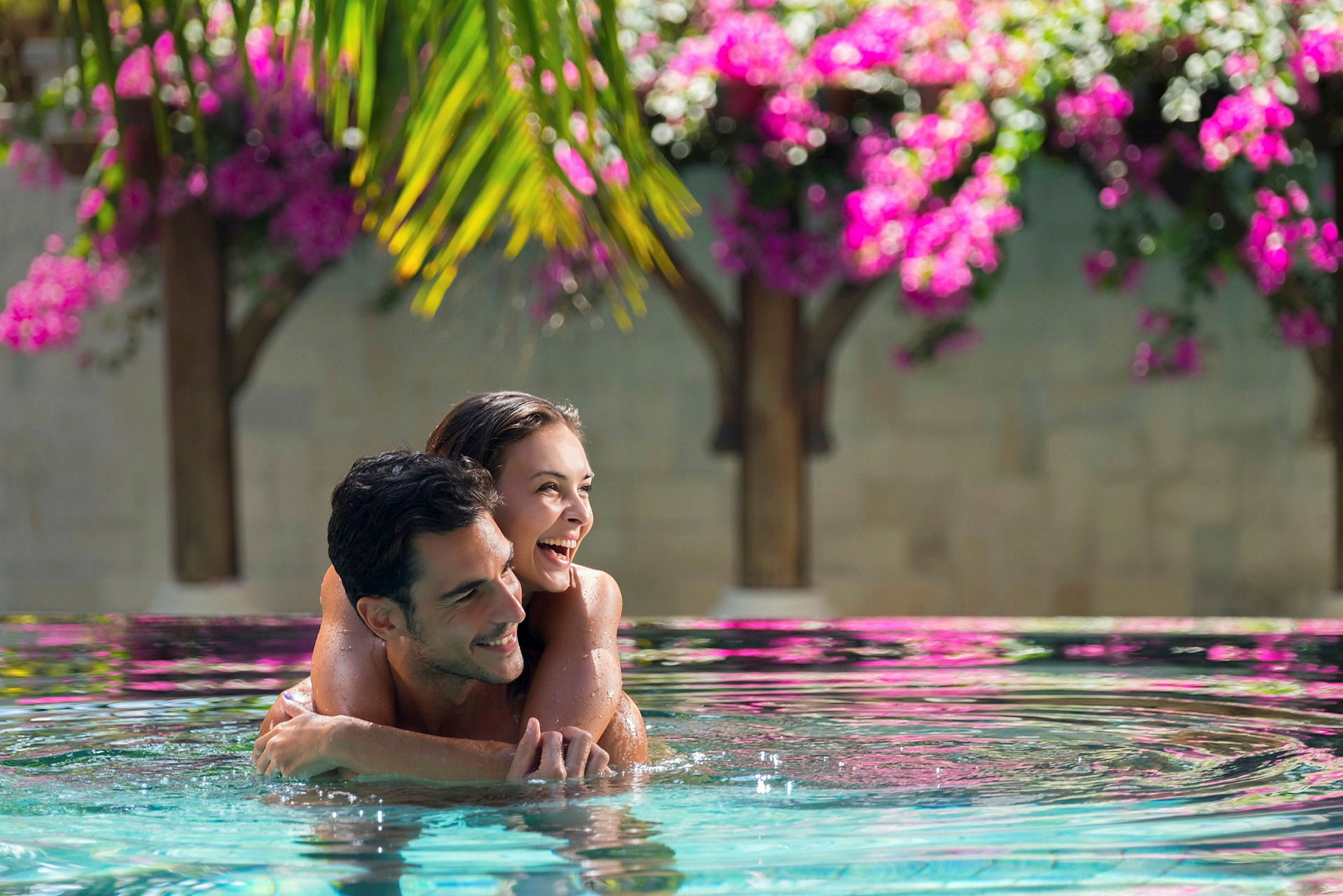 Två personer badar i en pool med blommor och vegetation i bakgrunden. (AI-genererad text)