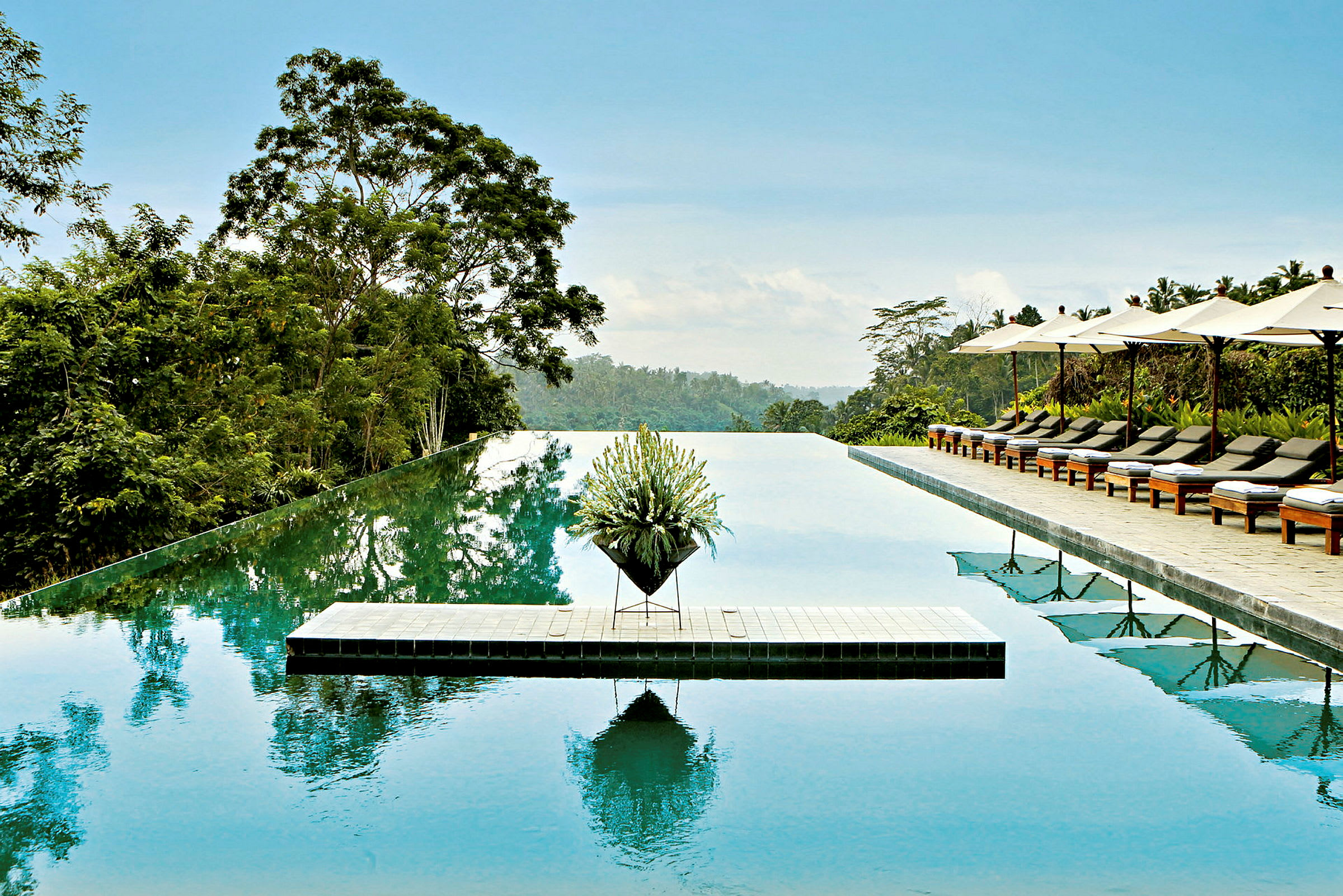 Infinitypool med grönskande omgivning, solstolar och parasoller till höger. (AI-genererad text)