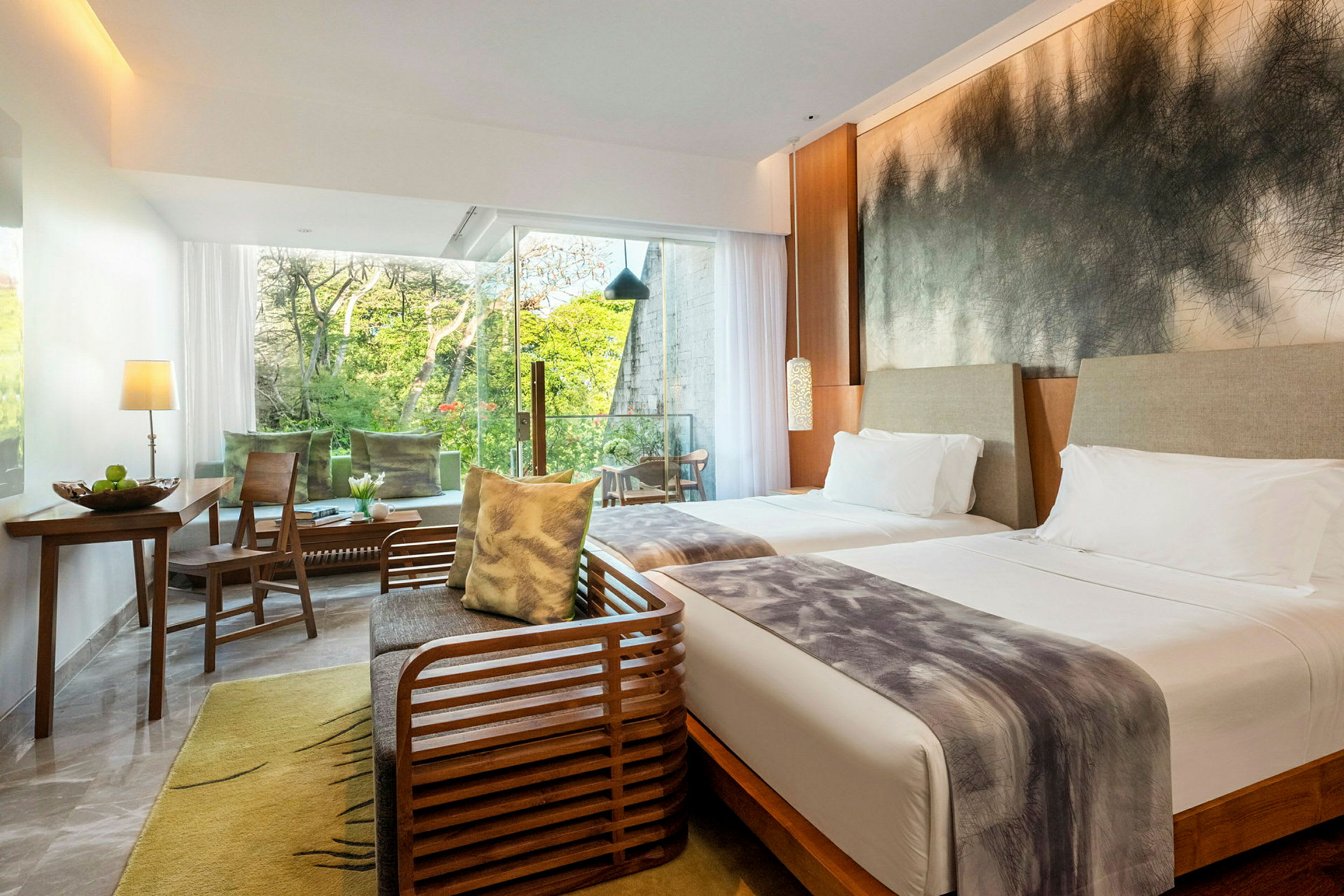 Ett hotellrum med två sängar, en sittgrupp, och stora fönster som släpper in ljus och ger utsikt över grönskande träd. (AI-genererad text)