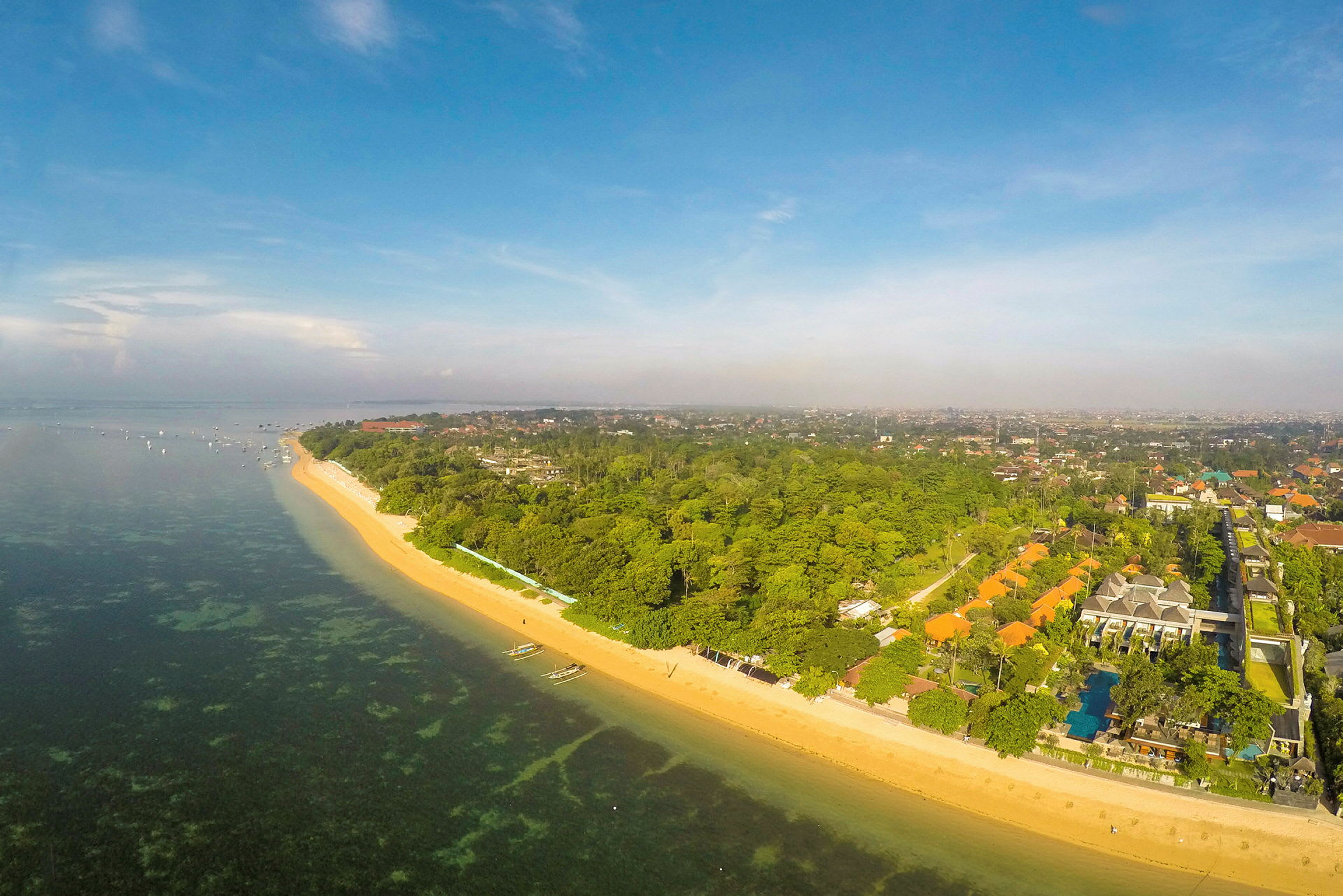 Flygfoto av en kustremsa med sandstrand, klart vatten och grönska i närheten. (AI-genererad text)