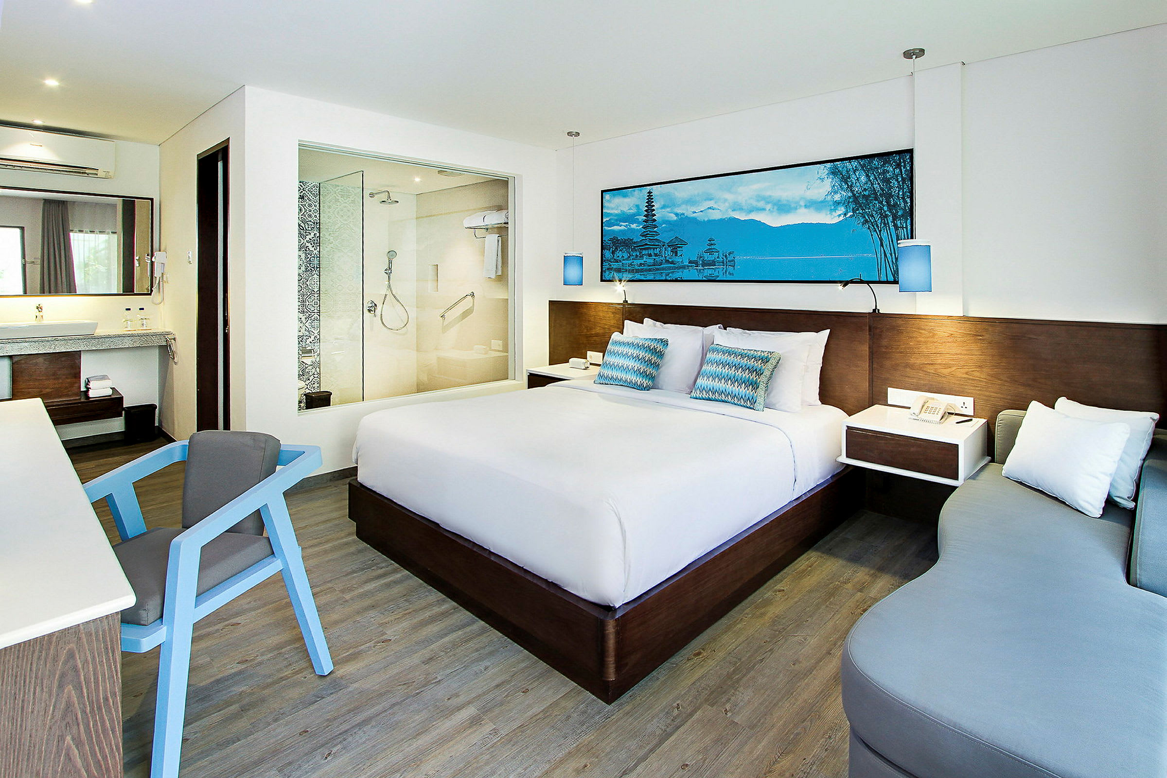 Ett modernt hotellrum med en stor säng, ett skrivbord med en stol, en soffa och ett badrum med glasvägg. (AI-genererad text)
