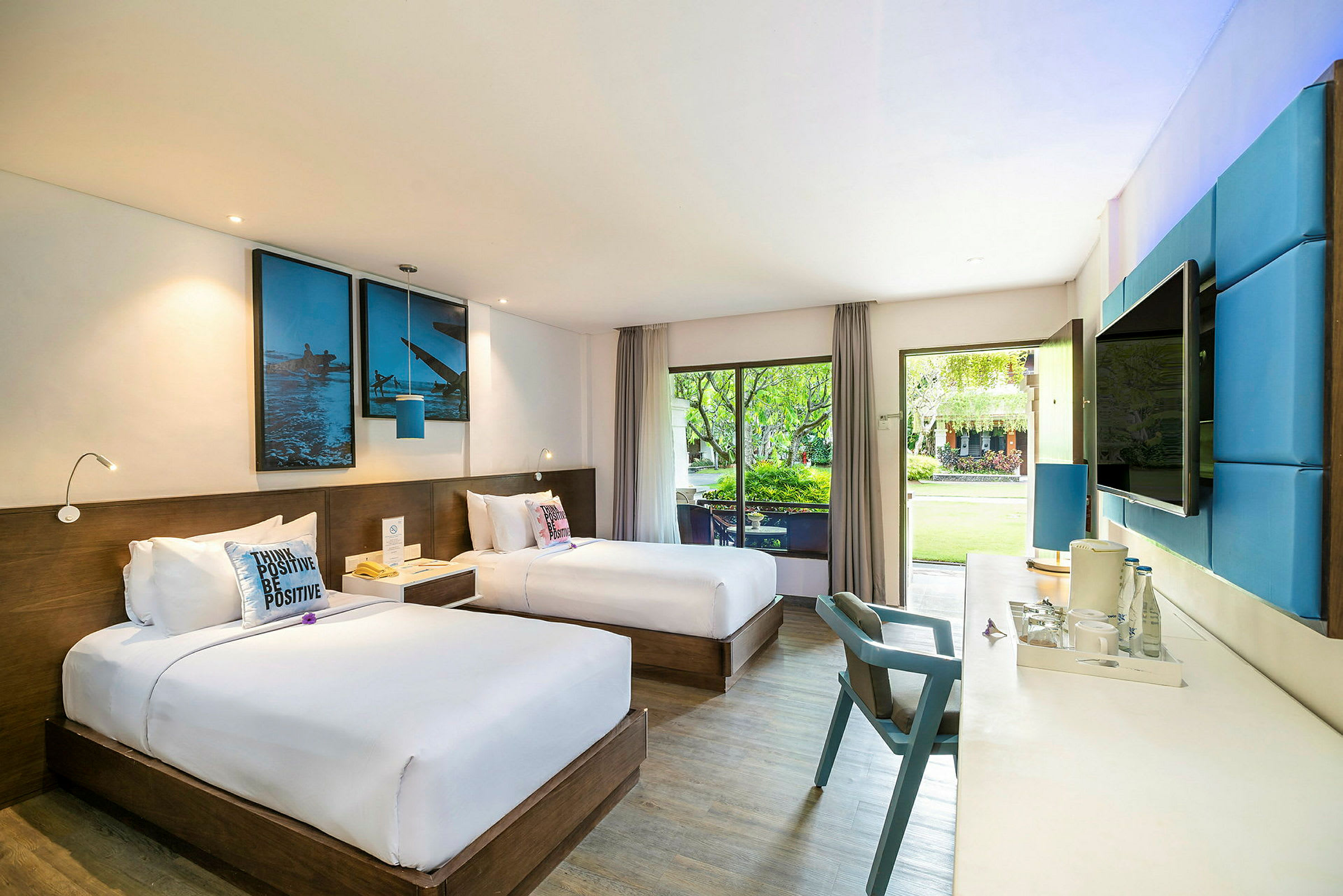 Ett hotellrum med två enkelsängar, modern inredning med blå detaljer, och stora fönster som vetter mot en trädgård. (AI-genererad text)