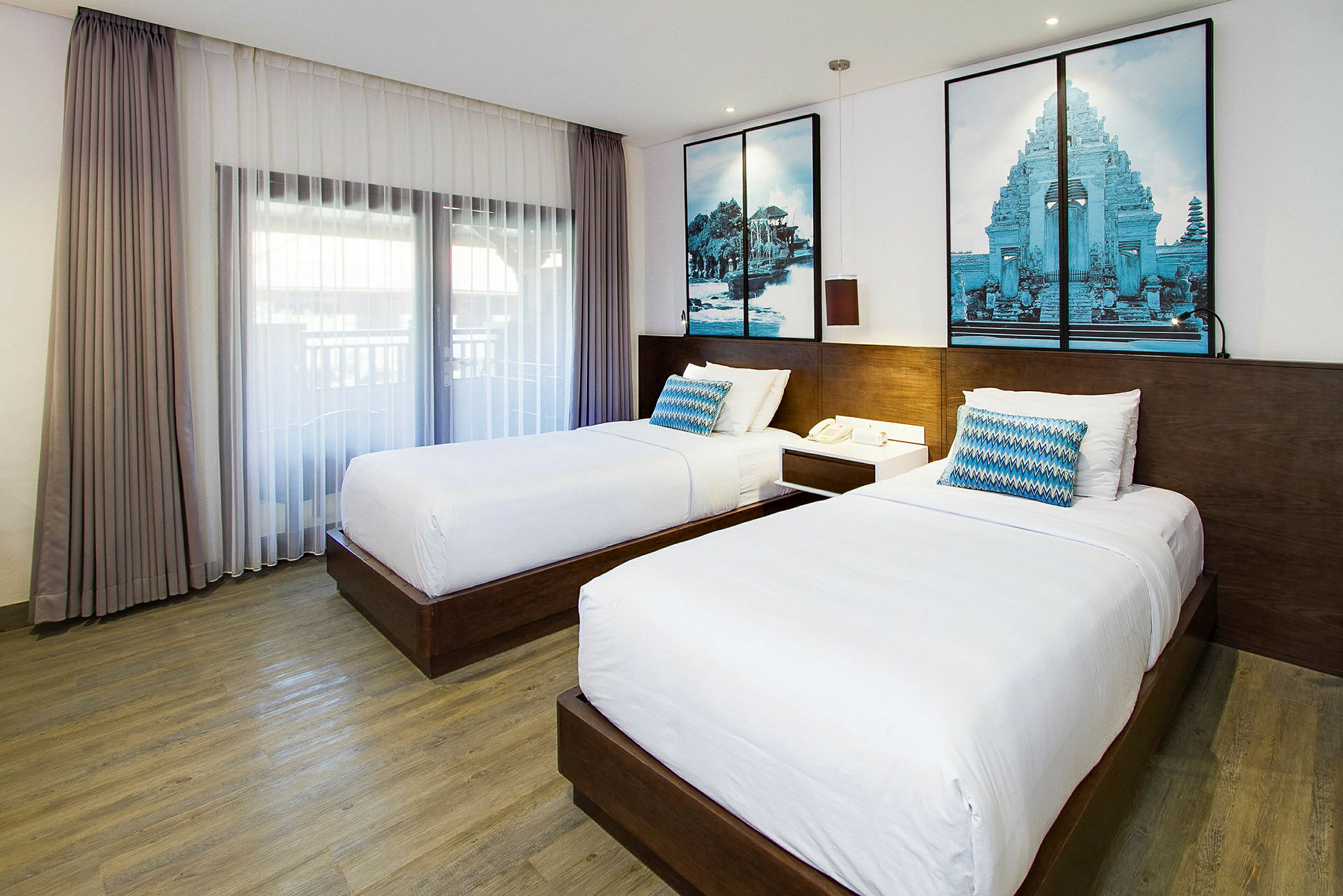 Ett hotellrum med två enkelsängar, en trägolv och stora fönster med gardiner. (AI-genererad text)