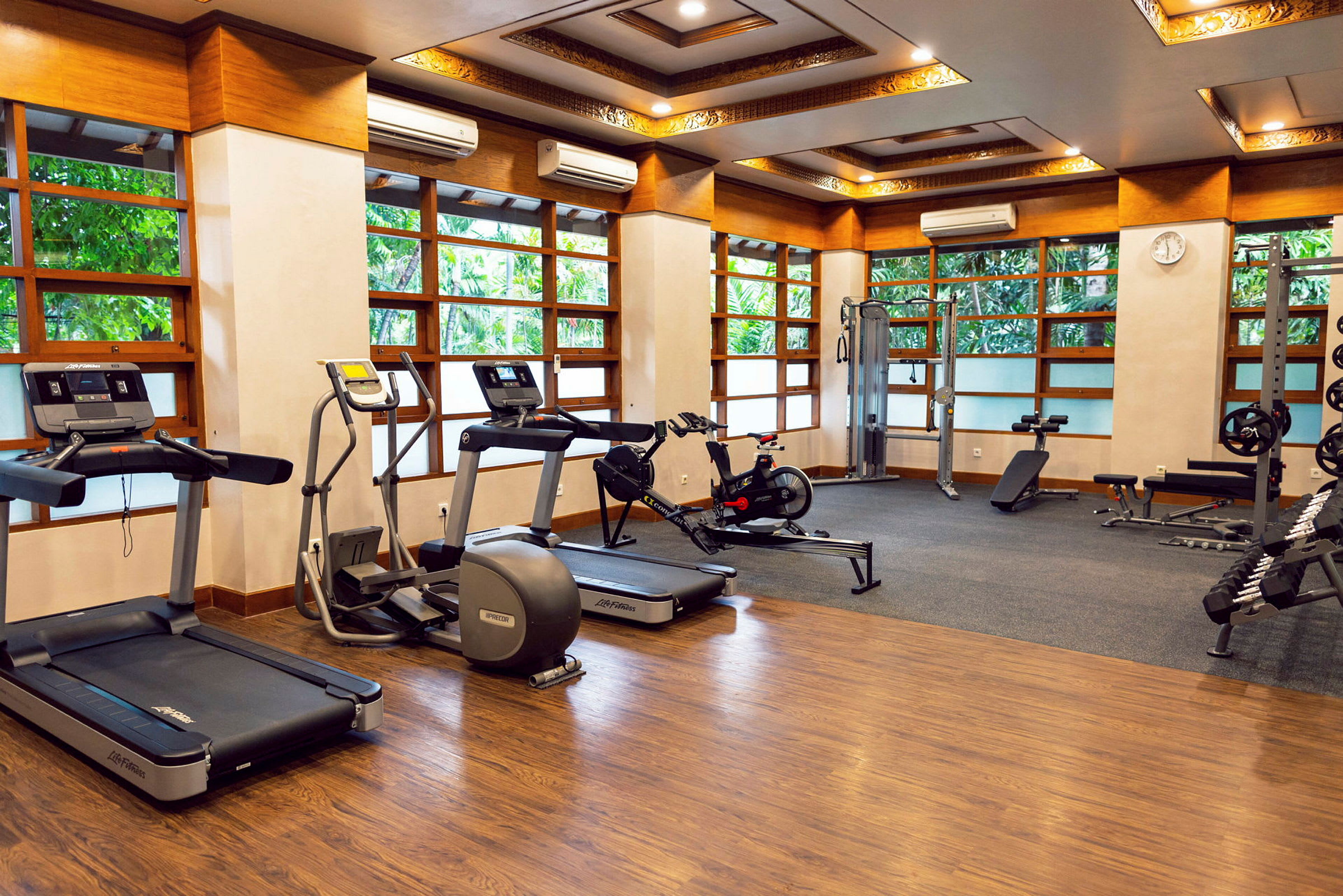 Ett gym med olika träningsmaskiner och fria vikter, med stora fönster som släpper in naturligt ljus. (AI-genererad text)