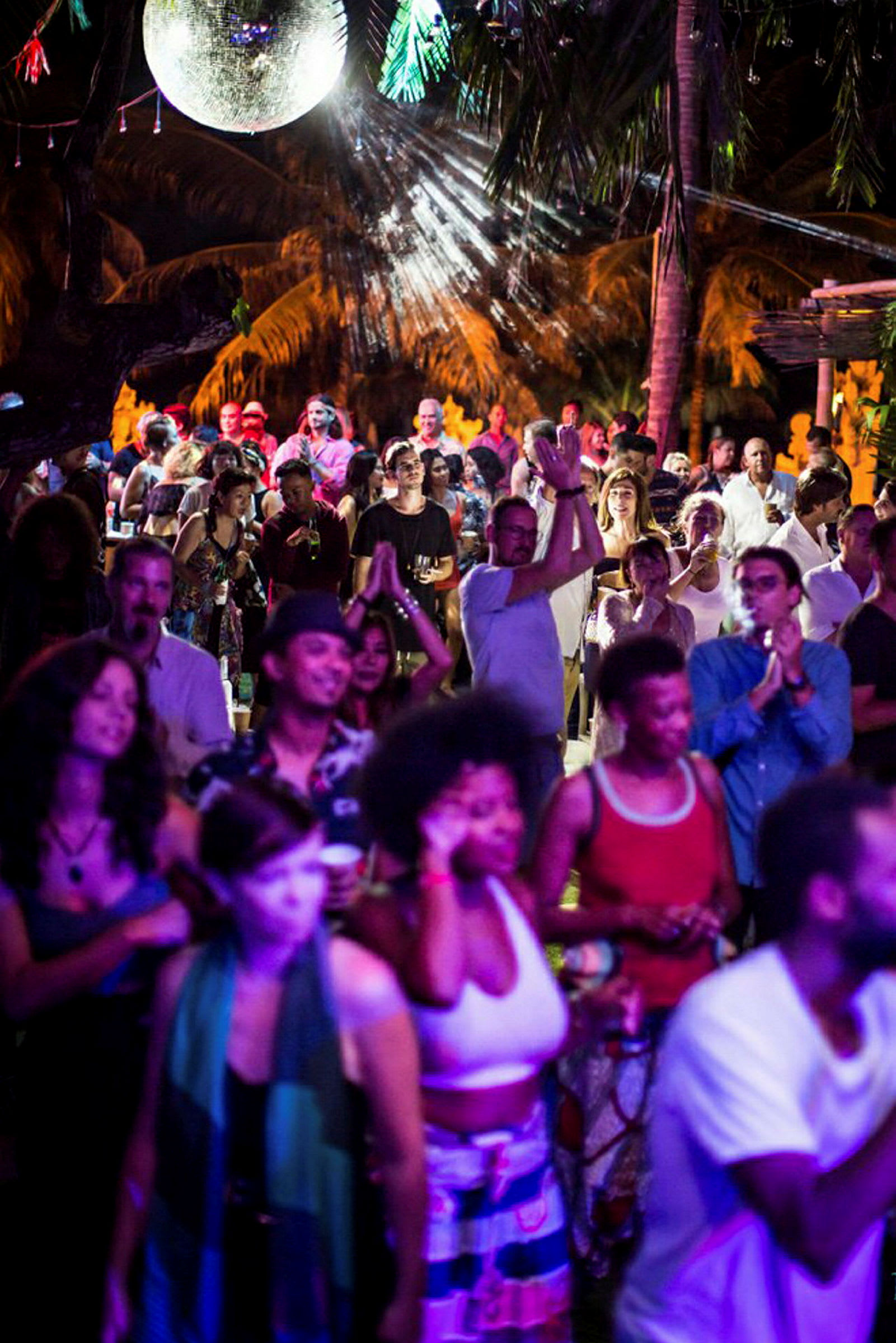 En nattklubbsmiljö utomhus med människor som dansar och en discokula i bakgrunden. (AI-genererad text)