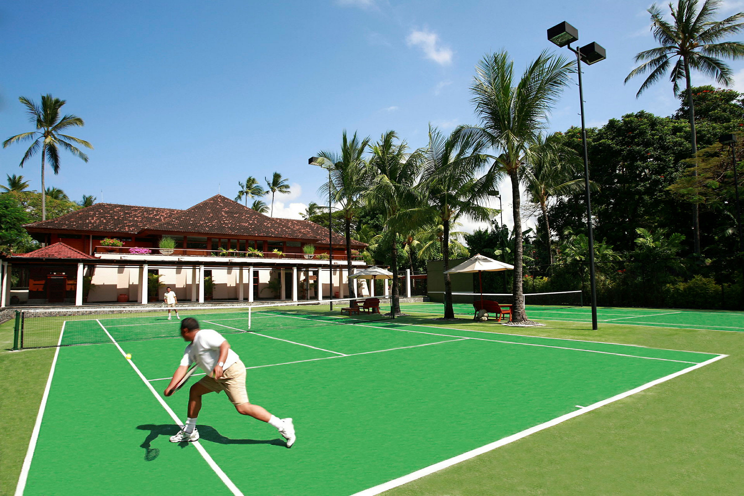 En grön tennisbana med palmer och byggnader i bakgrunden. (AI-genererad text)