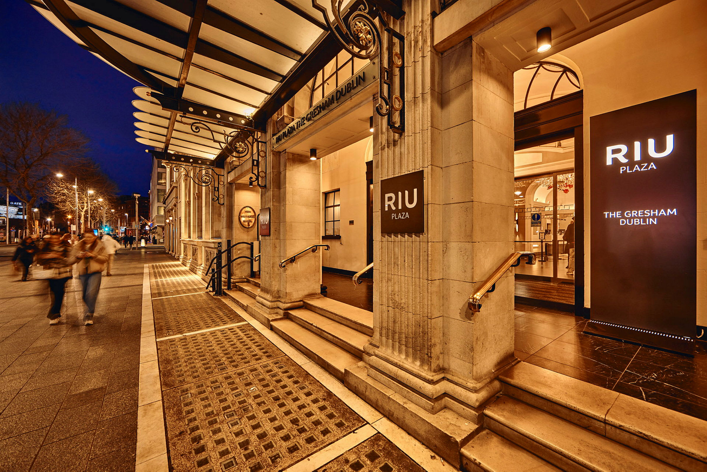Hotell RIU Plaza Gresham Dublin ingång med upplysta skyltar, kvällsmiljö. (AI-genererad text)