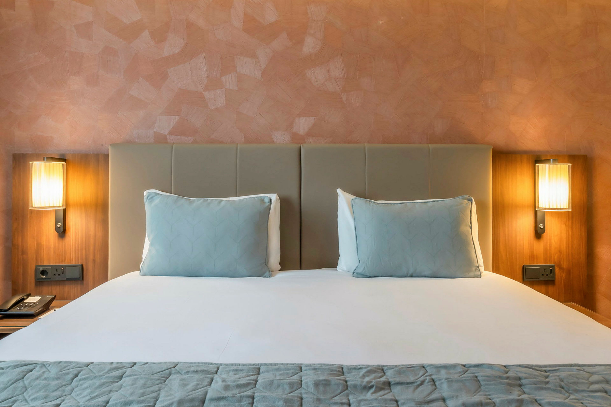 Hotellsäng med två kuddar och två nattduksbordslampor. (AI-genererad text)