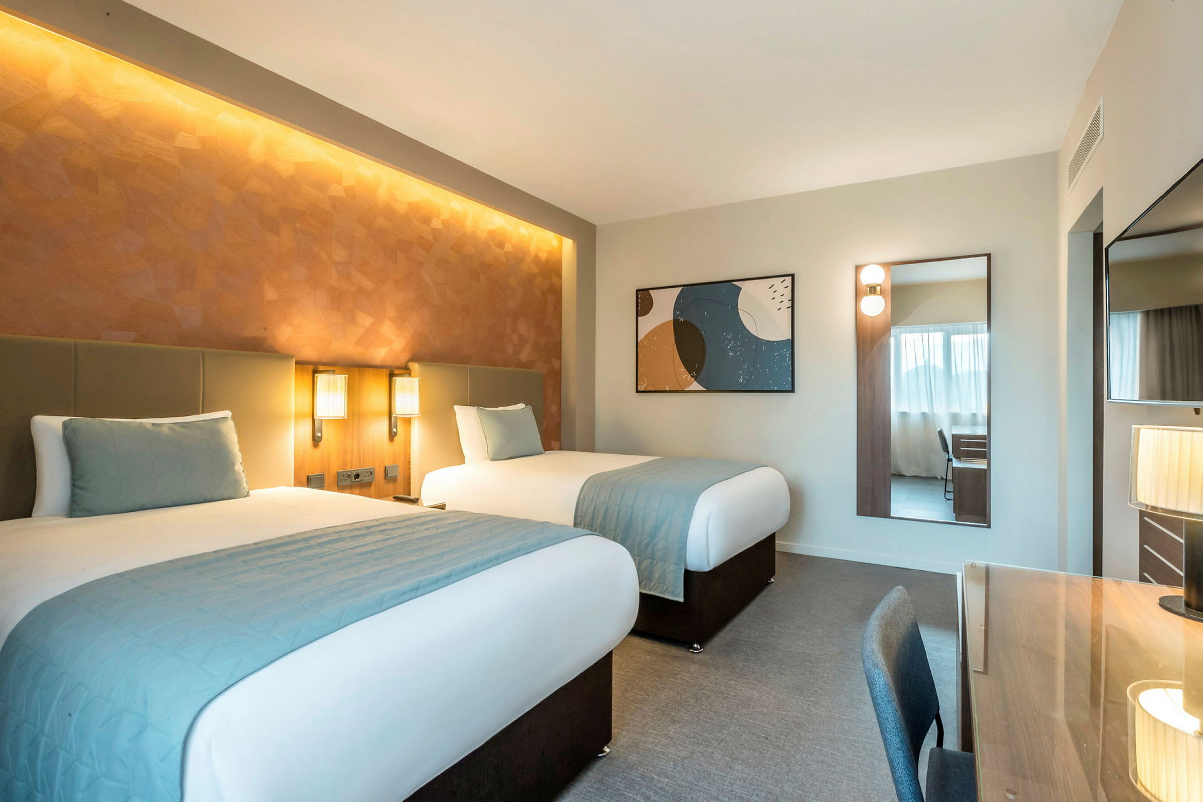 Hotellrum med två enkelsängar, skrivbord och spegel. (AI-genererad text)