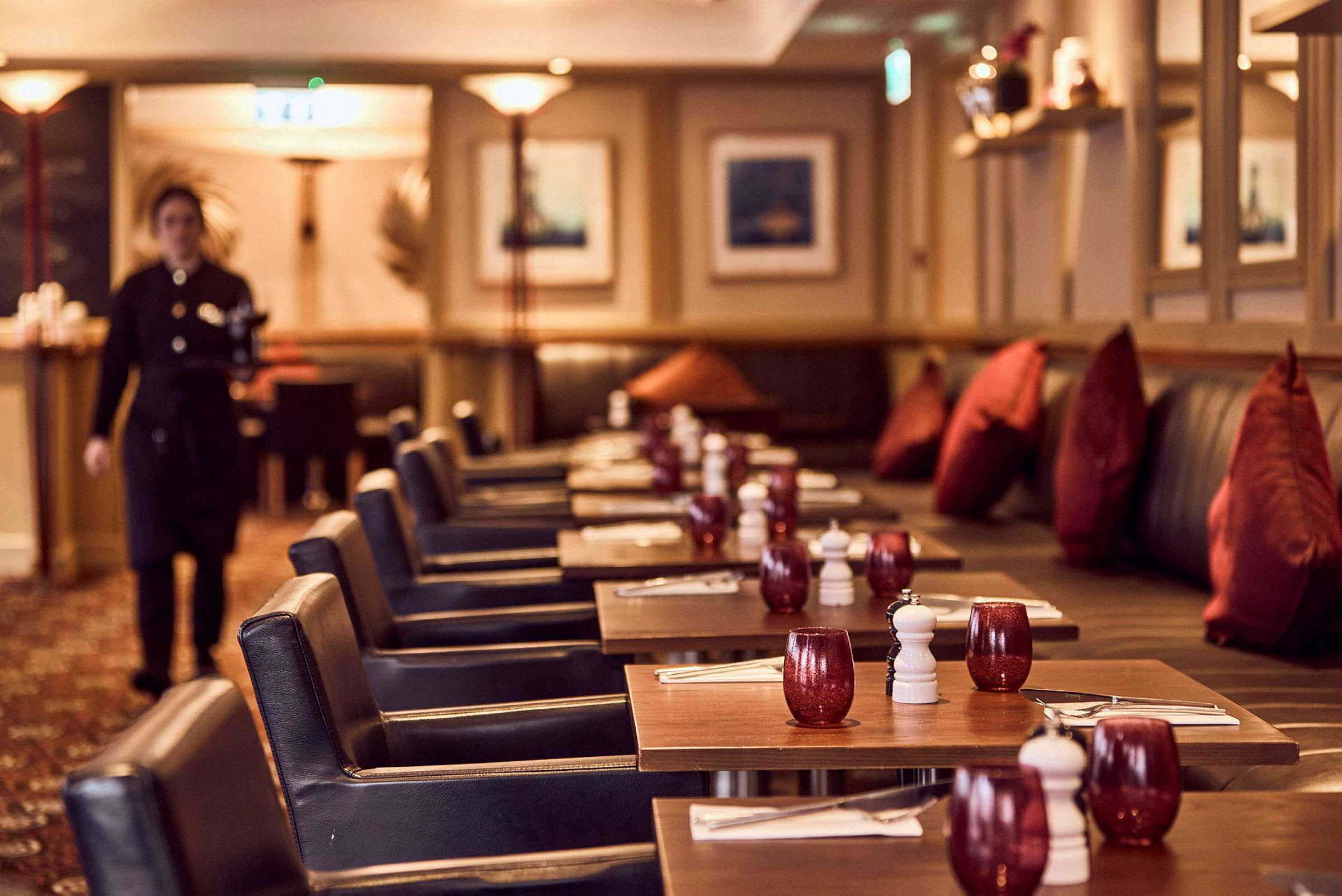 En restaurang med dukade bord, röda glas och mörka stolar syns i bilden. (AI-genererad text)