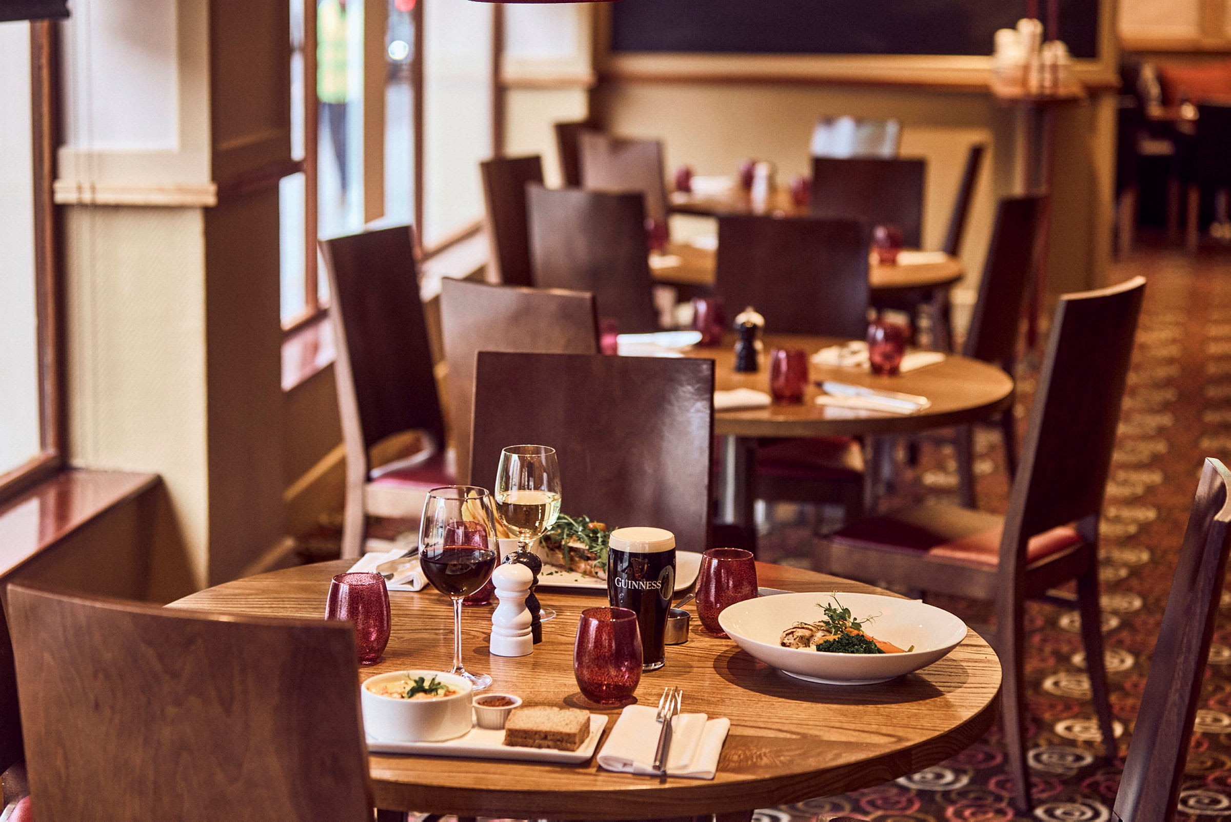 Ett restaurangbord med två glas vin och serverad mat på tallrikar. (AI-genererad text)