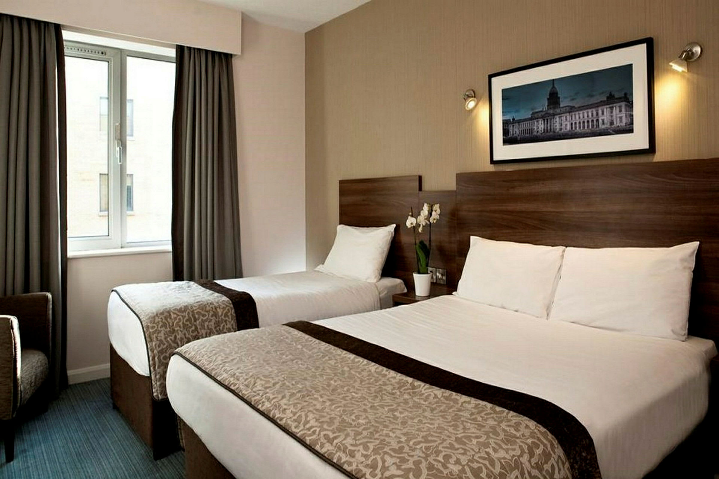 Hotellrum med två sängar, en växt på nattduksbordet, ett fönster och en väggdekoration. (AI-genererad text)
