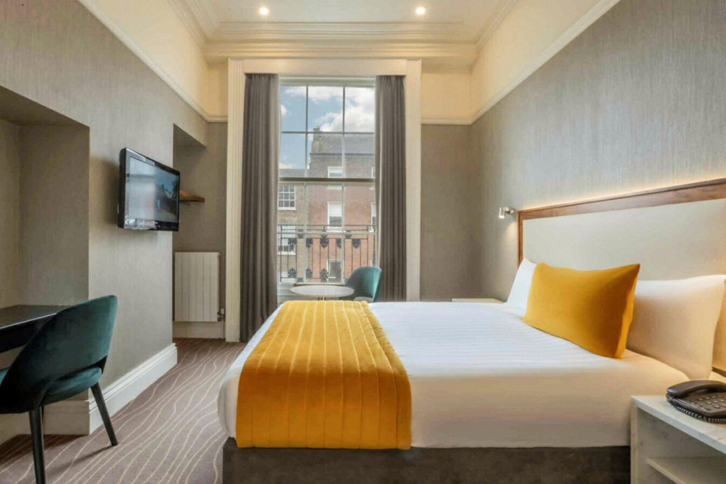Bild av ett hotellrum med en stor säng, gul sängklädsel, TV på väggen och en fönsterutsikt. (AI-genererad text)