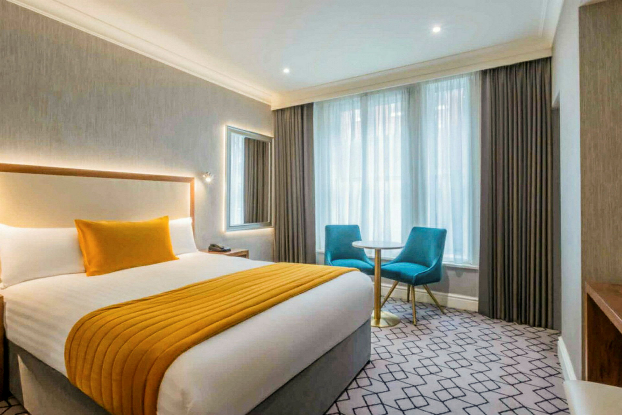 Hotellrum med en dubbelsäng, två blå stolar och ett litet bord vid fönstret. (AI-genererad text)