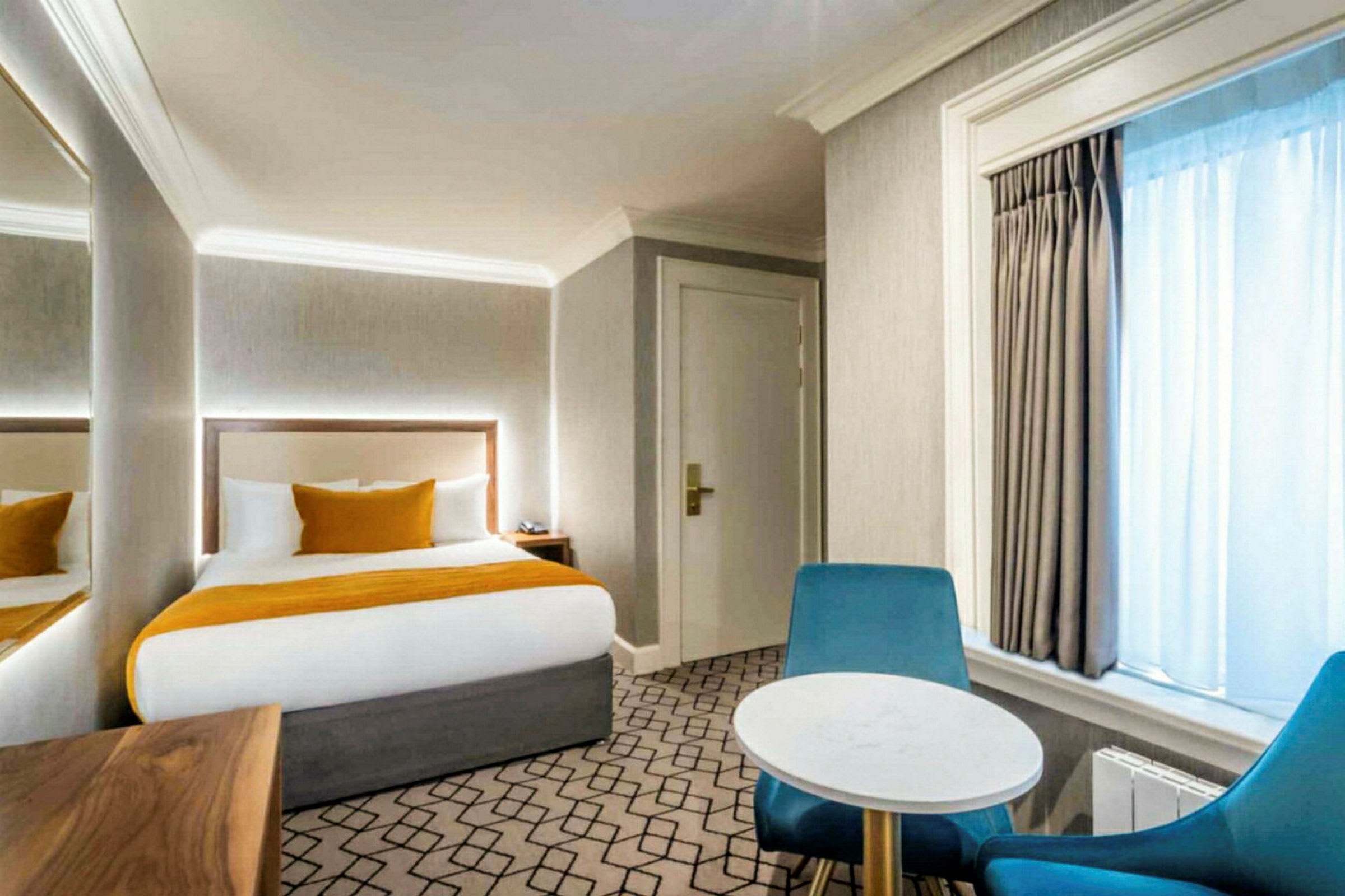 En hotellrum med en säng, två stolar och ett bord, samt naturligt ljus från ett fönster. (AI-genererad text)
