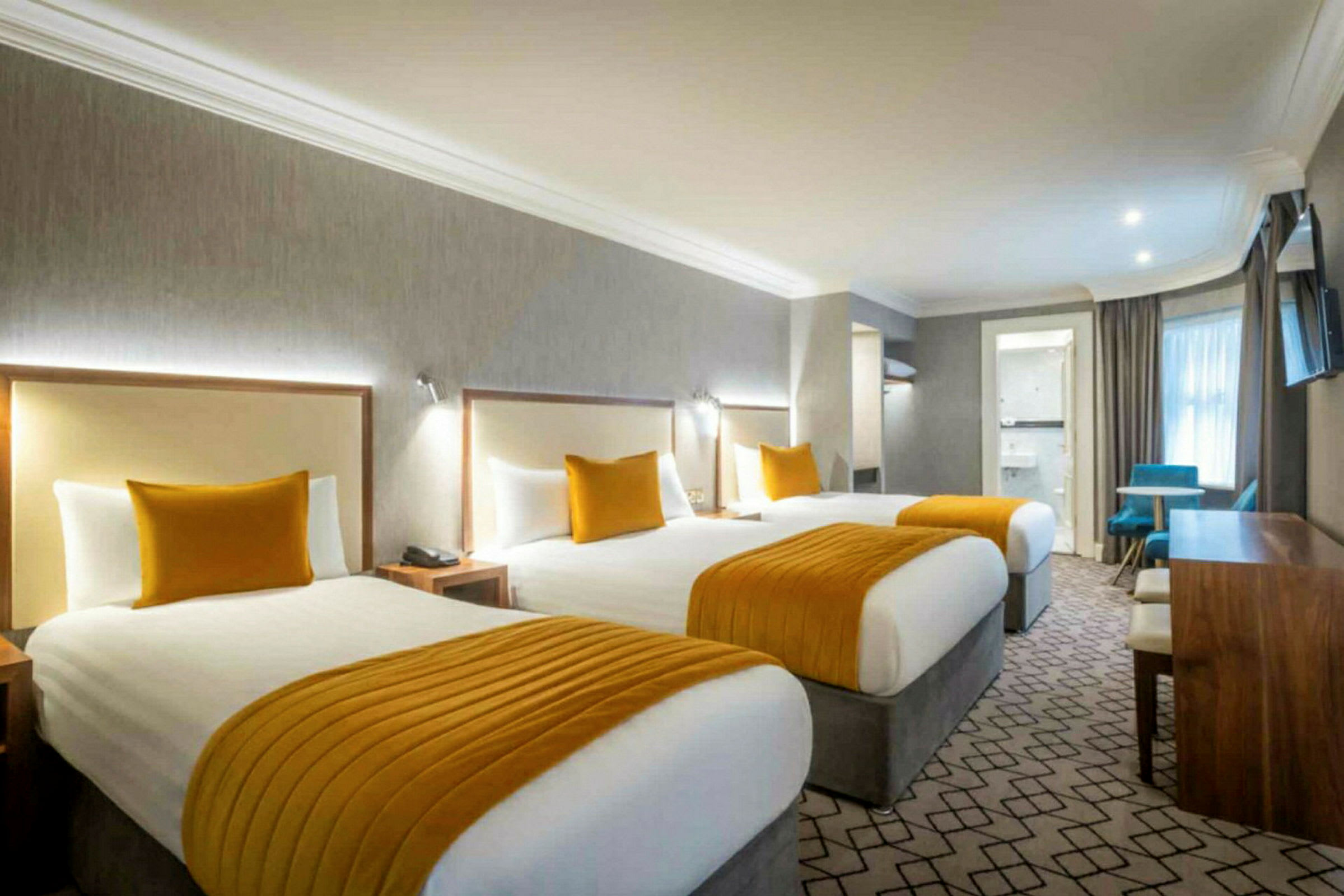 Hotellrum med tre bäddar, orange detaljer och skrivbord. (AI-genererad text)