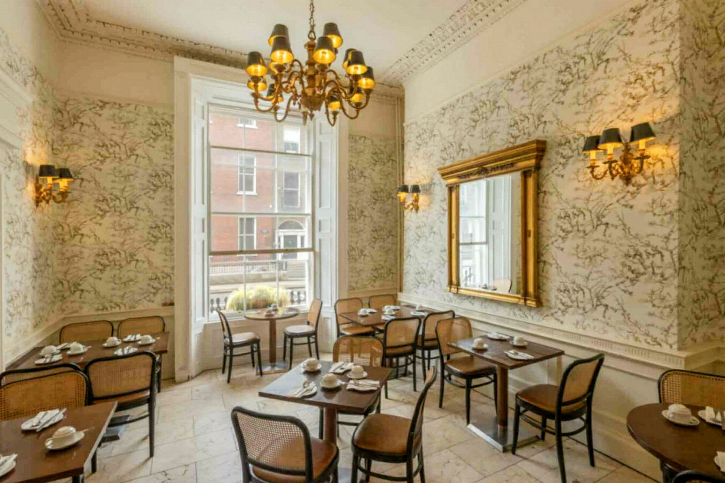 En restauranginteriör med klassisk inredning, bord och stolar, stor spegel och en ljuskrona. (AI-genererad text)