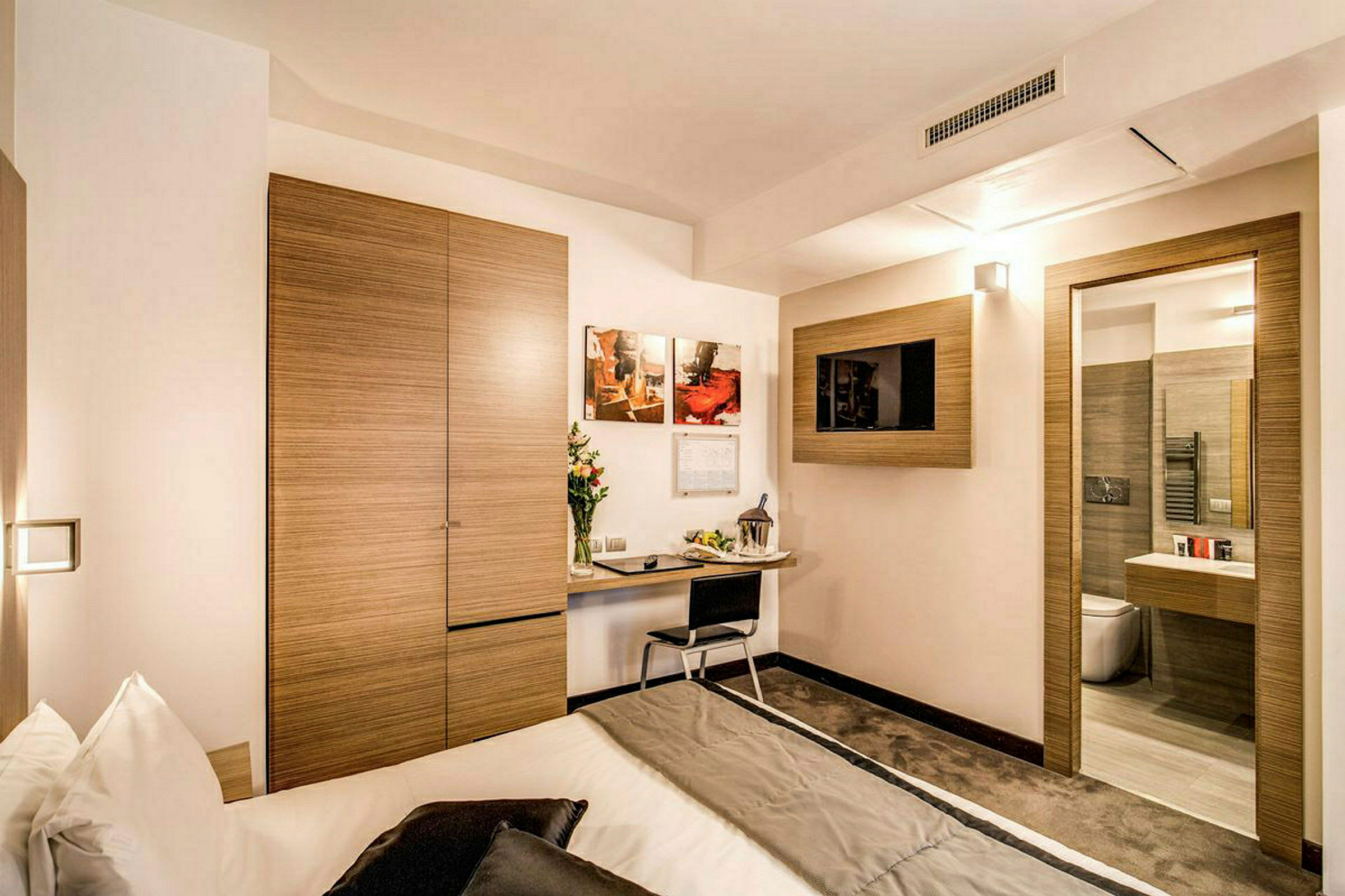 Ett modernt hotellrum med ett skrivbord, en säng och en tv på väggen. (AI-genererad text)