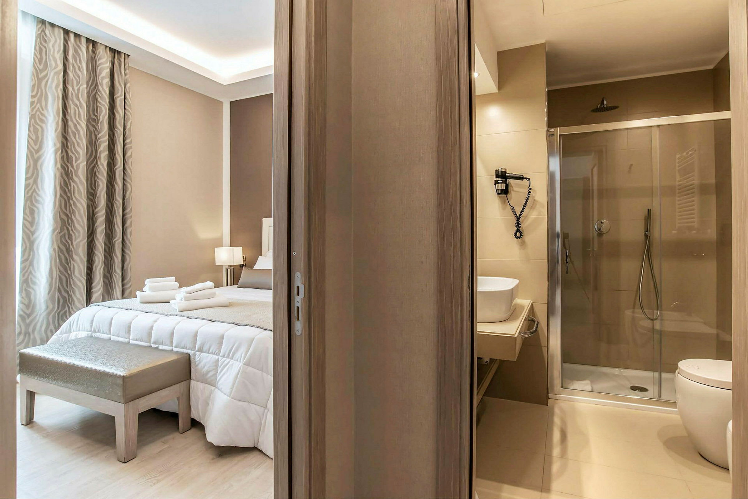 Hotellrum med en bred säng, inredd i ljusa toner, intill ett modernt badrum. (AI-genererad text)