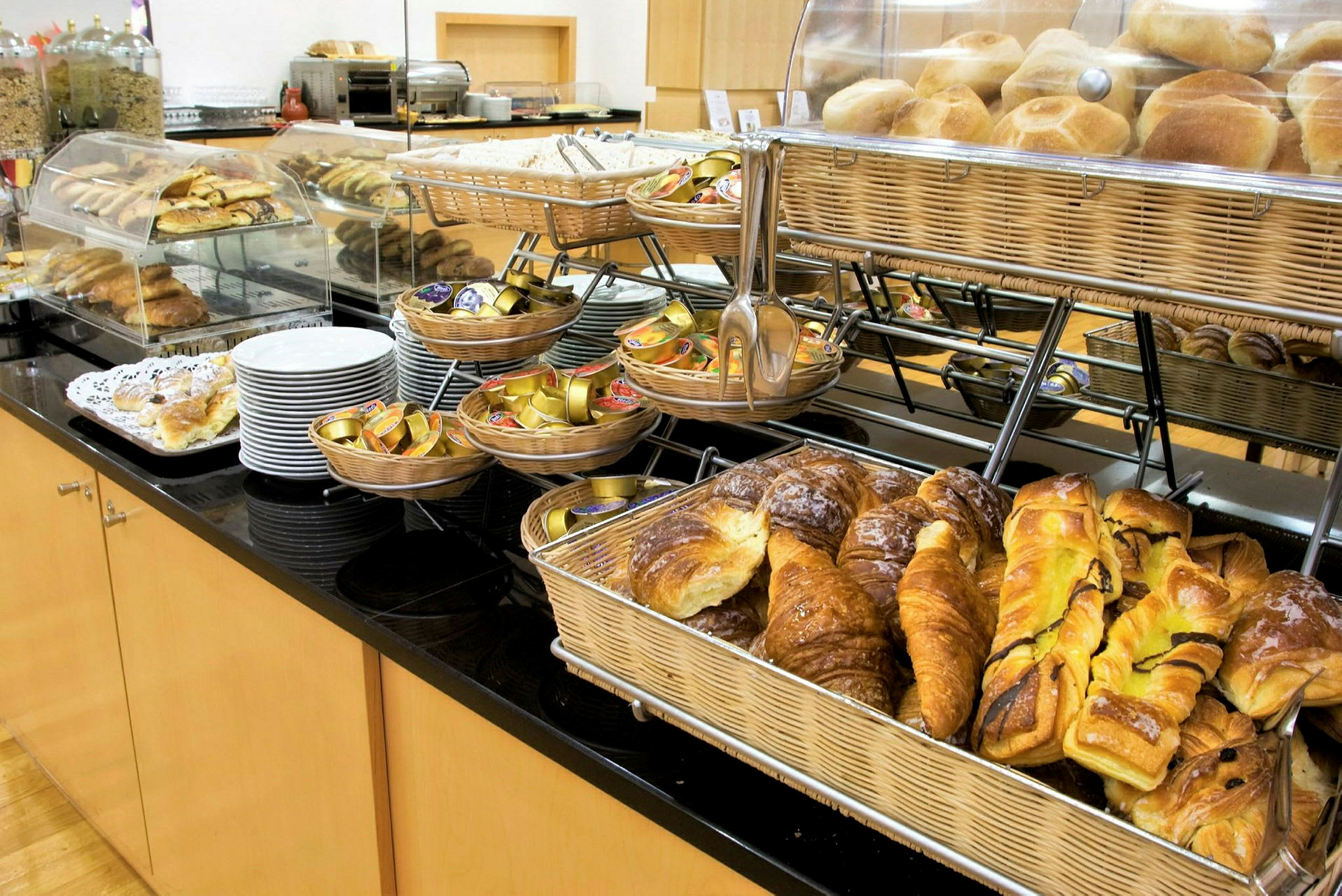 Ett frukostbuffébord med olika sorters bakverk, bröd i korgar och portioner av sylt. (AI-genererad text)