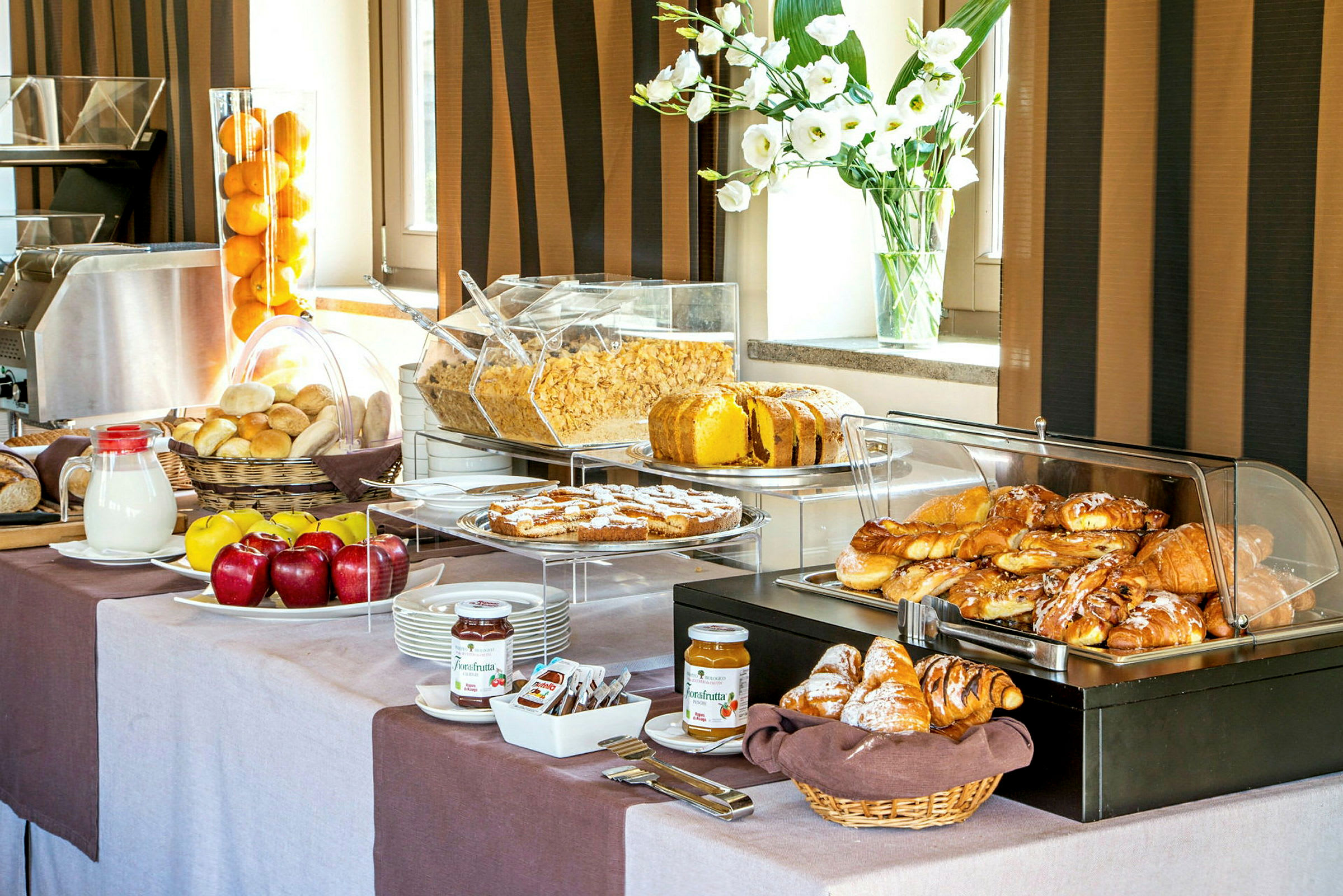 En buffé med frukostmat som färskt bröd, croissanter, frukt, flingor och olika pålägg. (AI-genererad text)